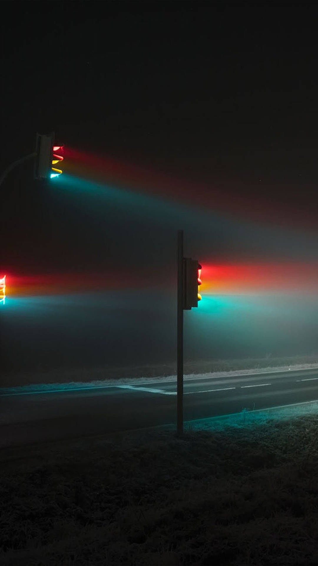 交通燈在寒冷的夜晚道路上透過薄霧發出紅色和青綠色的光芒。 — Oled 壁紙
