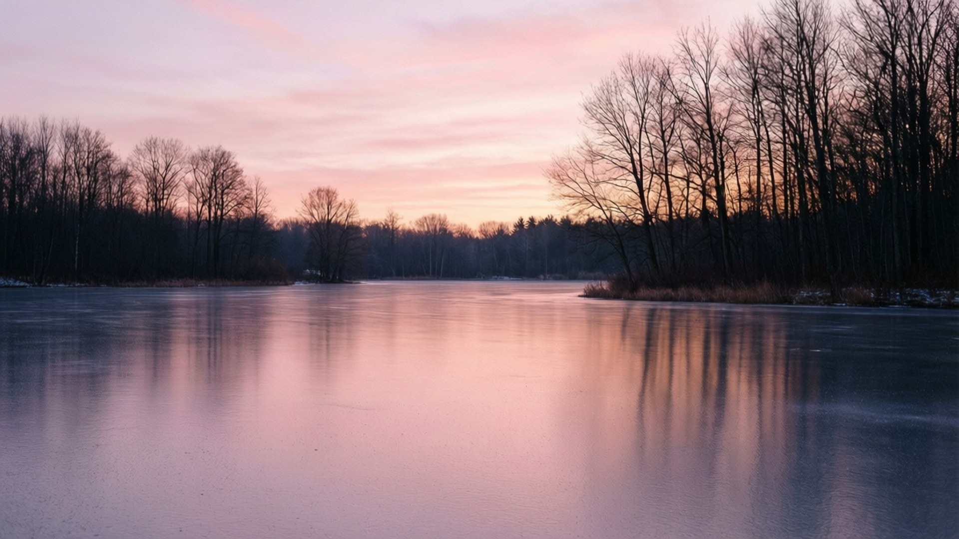 Frozen Lake Sunset 壁紙 — 黃昏時分的冰凍湖面反射出柔和的粉紅色和橙色天空，周圍是光禿禿的冬季樹木。