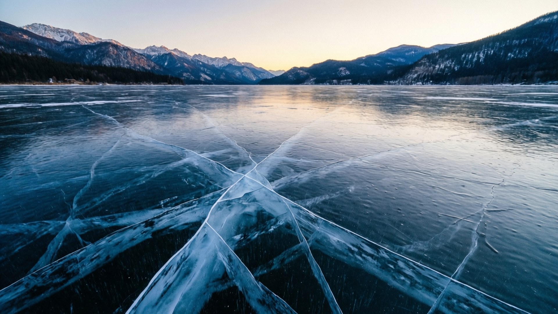 Frozen Lake Sunset 壁紙 — 一個結冰的湖面，帶有複雜的冰裂紋，在柔和的金色日落中延伸向積雪覆蓋的山脈。