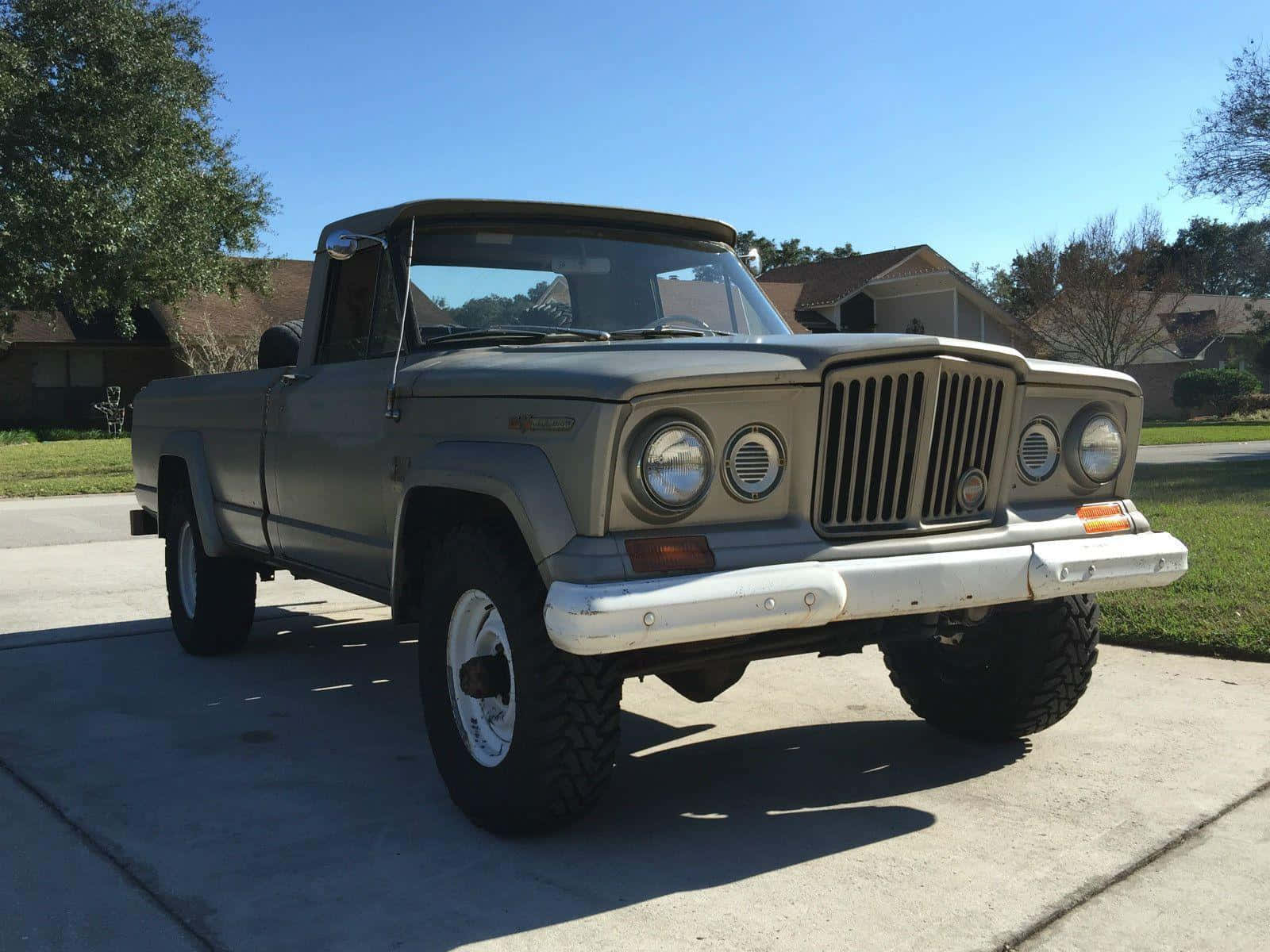 Jeep Gladiator 桌布 壁紙 — 一輛復古橄欖綠色的Jeep皮卡車，帶有白色保險桿和大輪胎，停在陽光明媚的混凝土車道上。