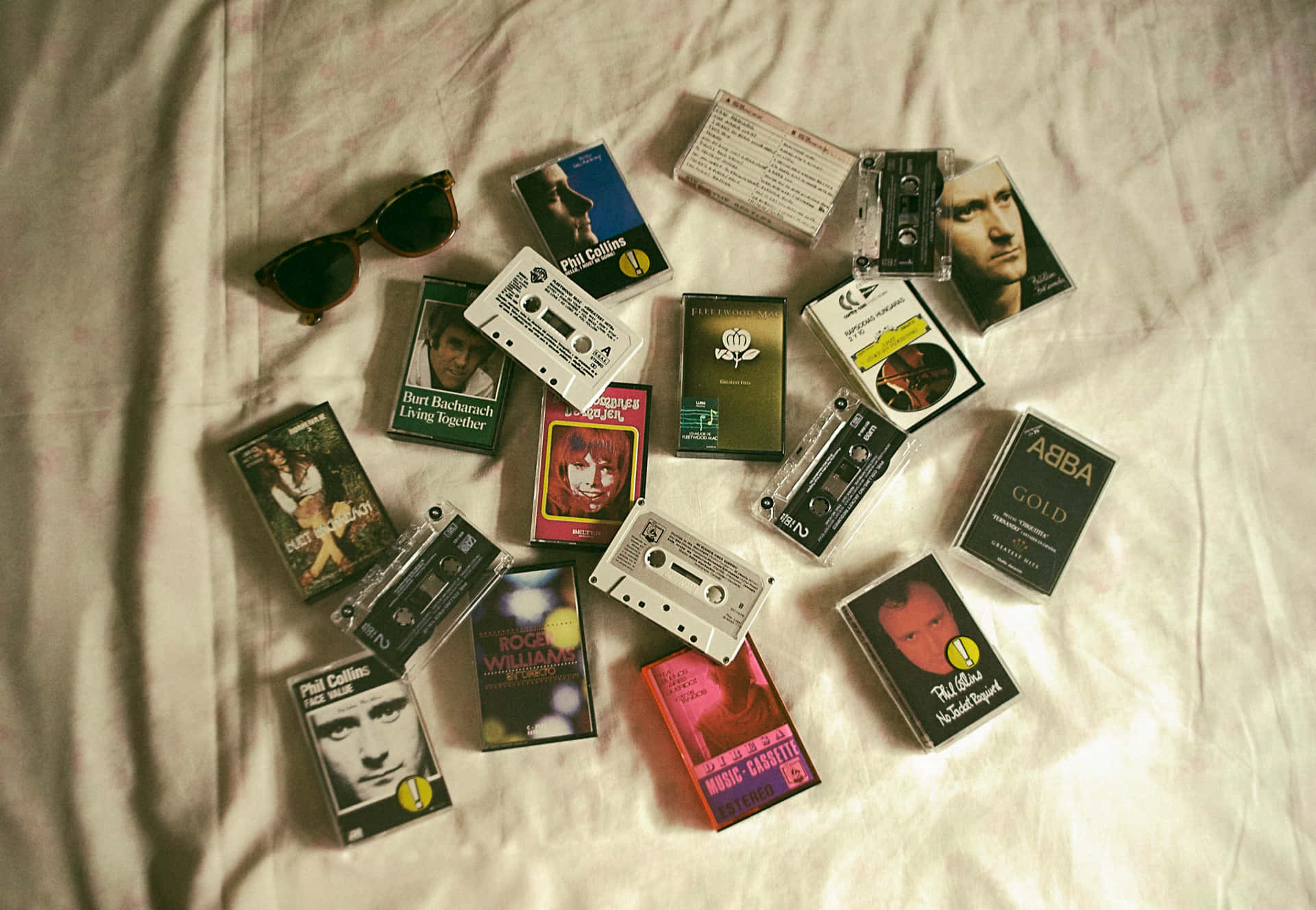  壁紙 — 復古卡式錄音帶和太陽眼鏡散落在溫暖燈光下的皺白床單上。