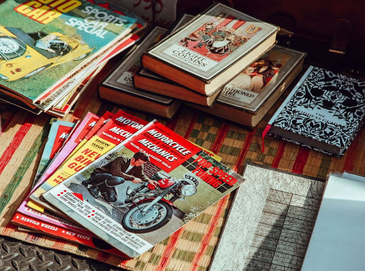 壁紙 — 復古汽車雜誌和書籍堆疊在條紋地毯上，沐浴在溫暖的陽光中。