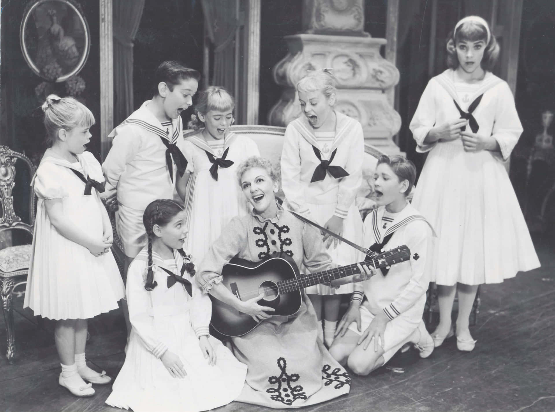  壁紙 — 一張復古黑白照片，一名女子彈吉他，周圍穿著水手服的孩子們露出驚訝的表情。