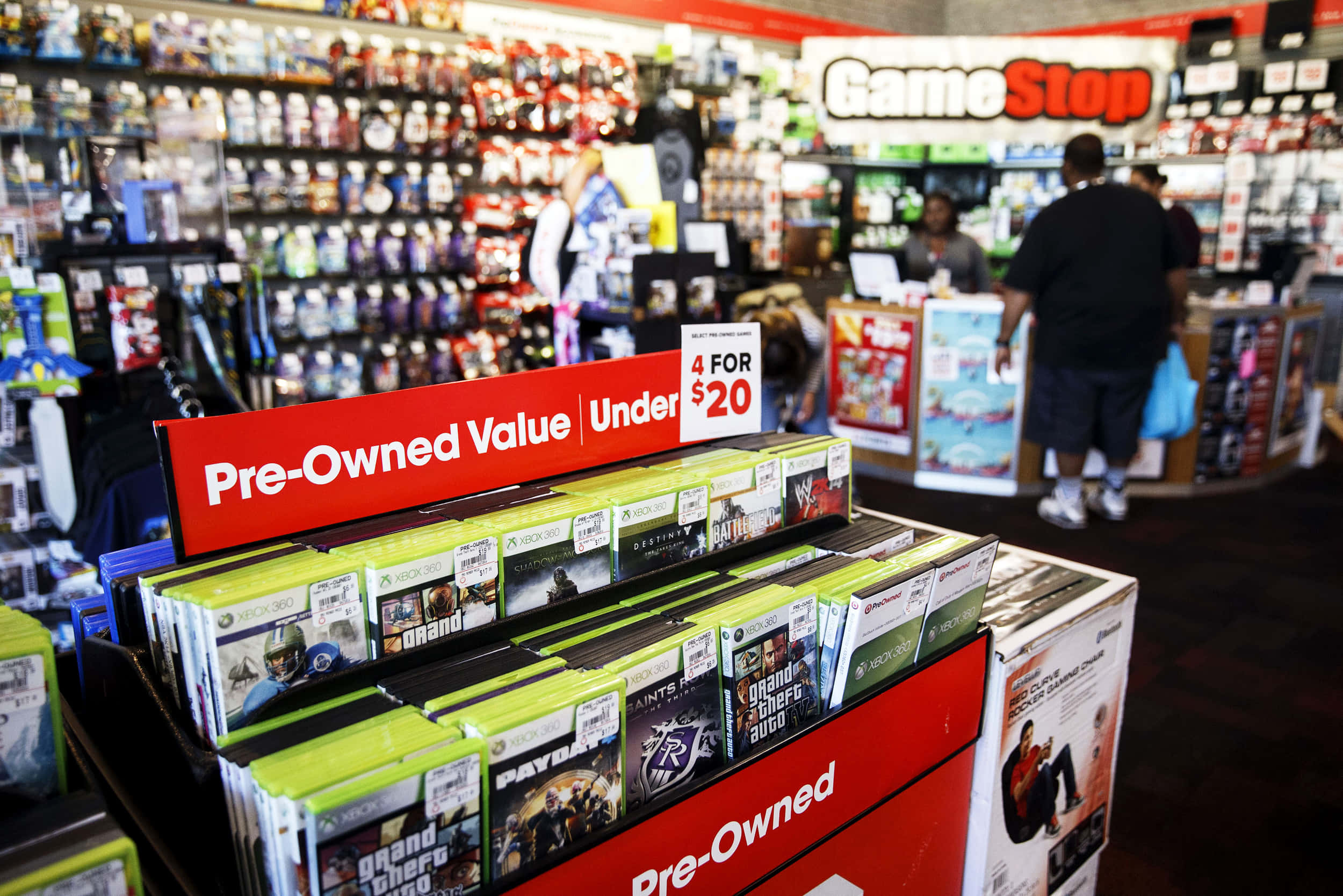 GameStop 桌布 壁紙 — GameStop 商店的貨架上展示著二手 Xbox 遊戲，紅色標誌宣傳四款遊戲低於二十美元。