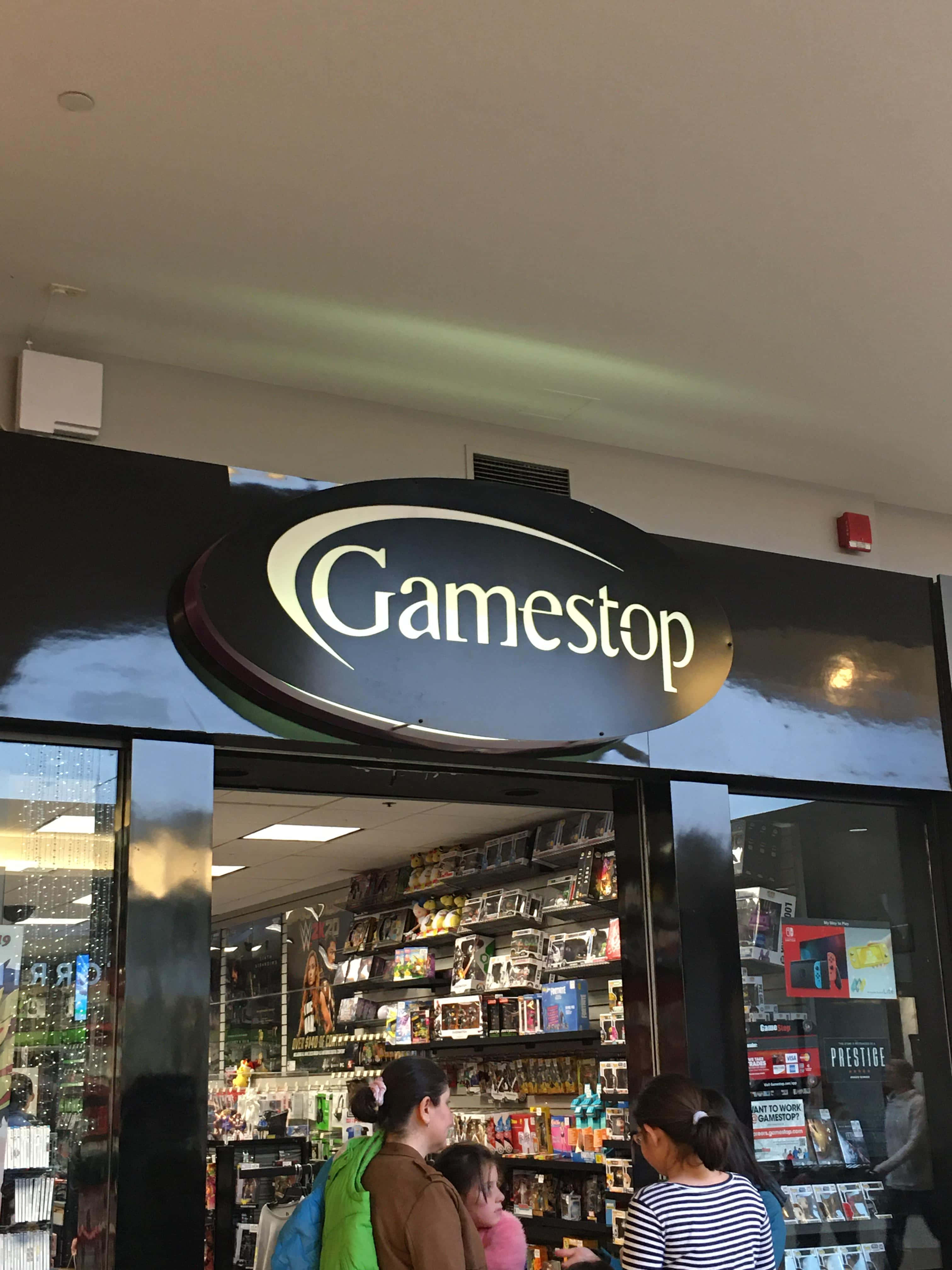 GameStop 桌布 壁紙 — GameStop 店鋪入口，購物者在明亮的螢光燈下瀏覽電玩遊戲和商品。