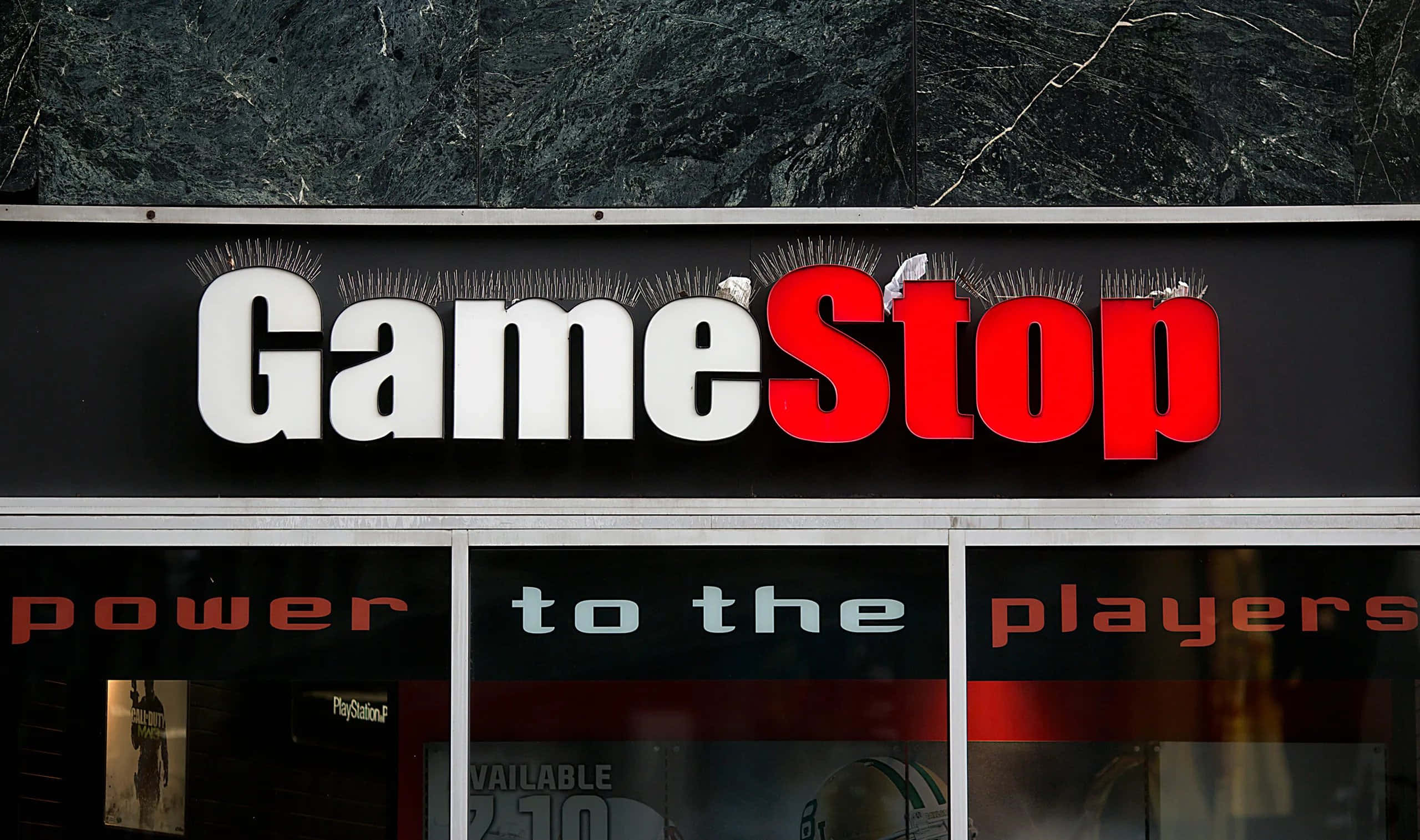 GameStop 桌布 壁紙 — GameStop 店鋪招牌，以粗體紅白字體顯示，背景為深色紋理牆壁。
