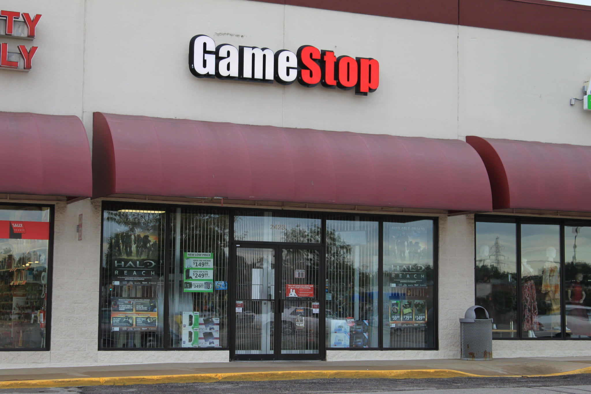 GameStop 桌布 壁紙 — GameStop 店鋪正面，紅色遮陽篷和玻璃門展示 Halo Reach 海報和價格標籤。