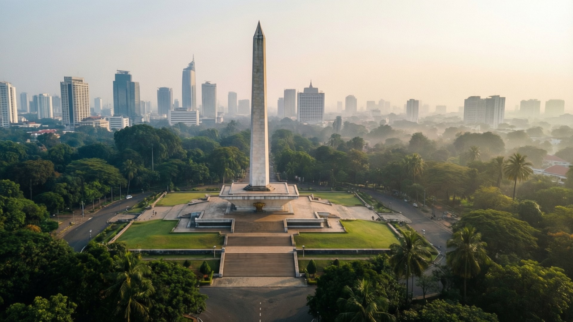 Monas from Above 壁紙 — 一座高聳的白色方尖碑紀念碑矗立在修剪整齊的綠色廣場中央，周圍環繞著茂密的樹木，背景是朦朧的現代城市天際線。
