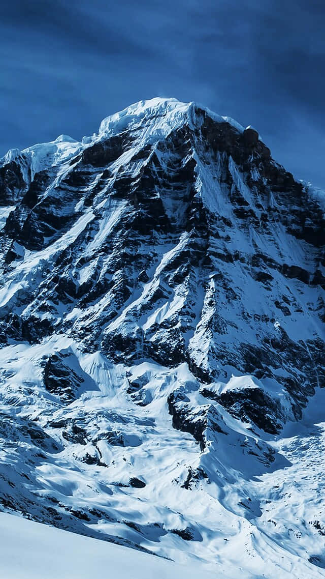  壁紙 — 高聳的雪山山峰在深藍色天空下尖銳地升起，戲劇性的陰影凸顯其崎嶇的質感。