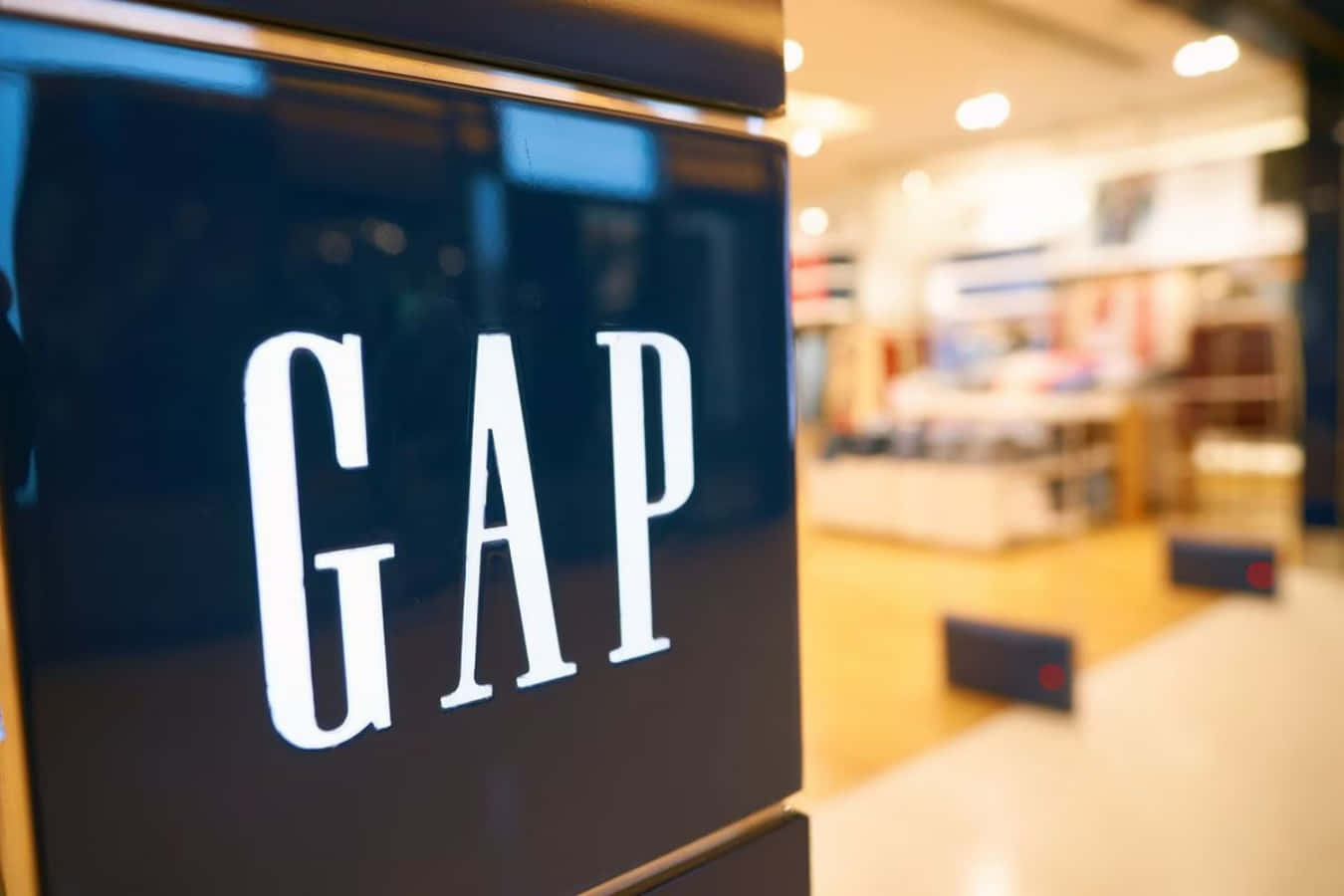Gap 桌布 壁紙 — GAP 商店標誌的特寫，發出光芒，背後是柔和模糊的暖色調零售店內部。