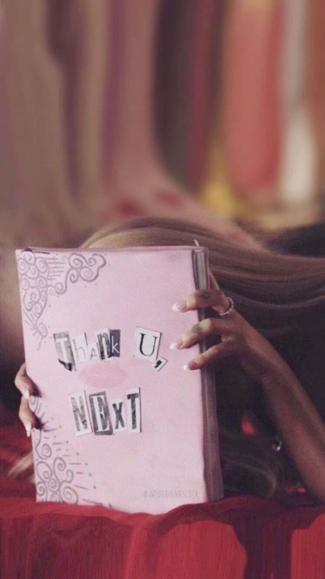 壁紙 — 一個長髮的人，在溫暖的燈光下，將一張粉紅色的專輯《Thank U, Next》放在臉前。