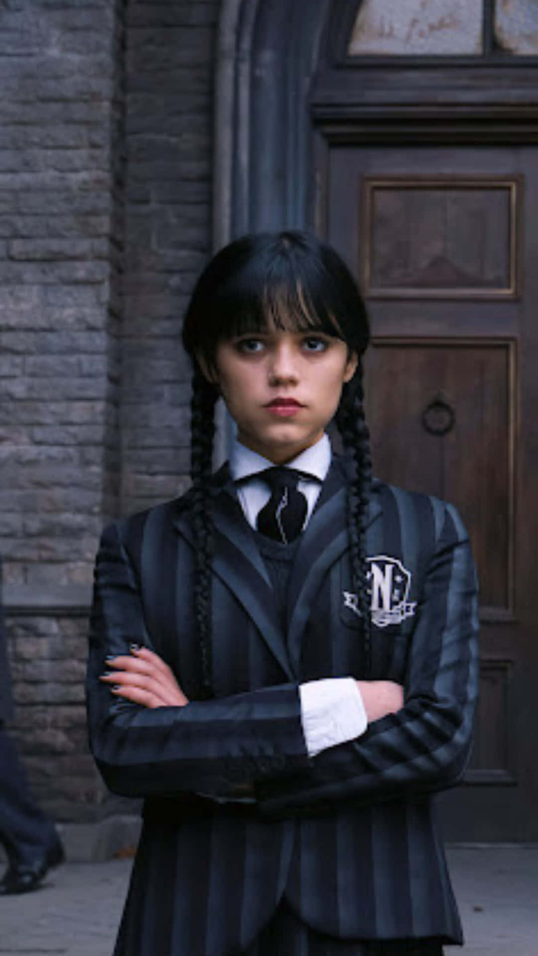  壁紙 — 一個穿著黑白條紋校服的年輕女孩，雙臂交叉站在石造建築物前。