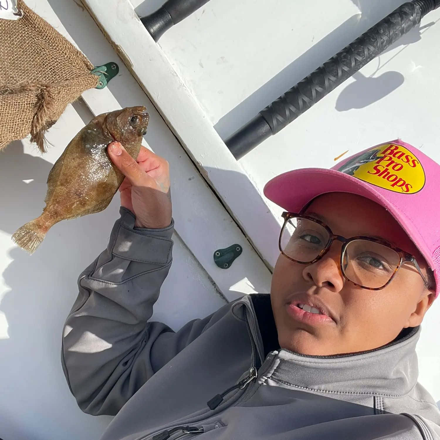  壁紙 — 一個戴粉紅色帽子的人在晴朗天空下的白色船上拿著一條剛捕獲的比目魚。