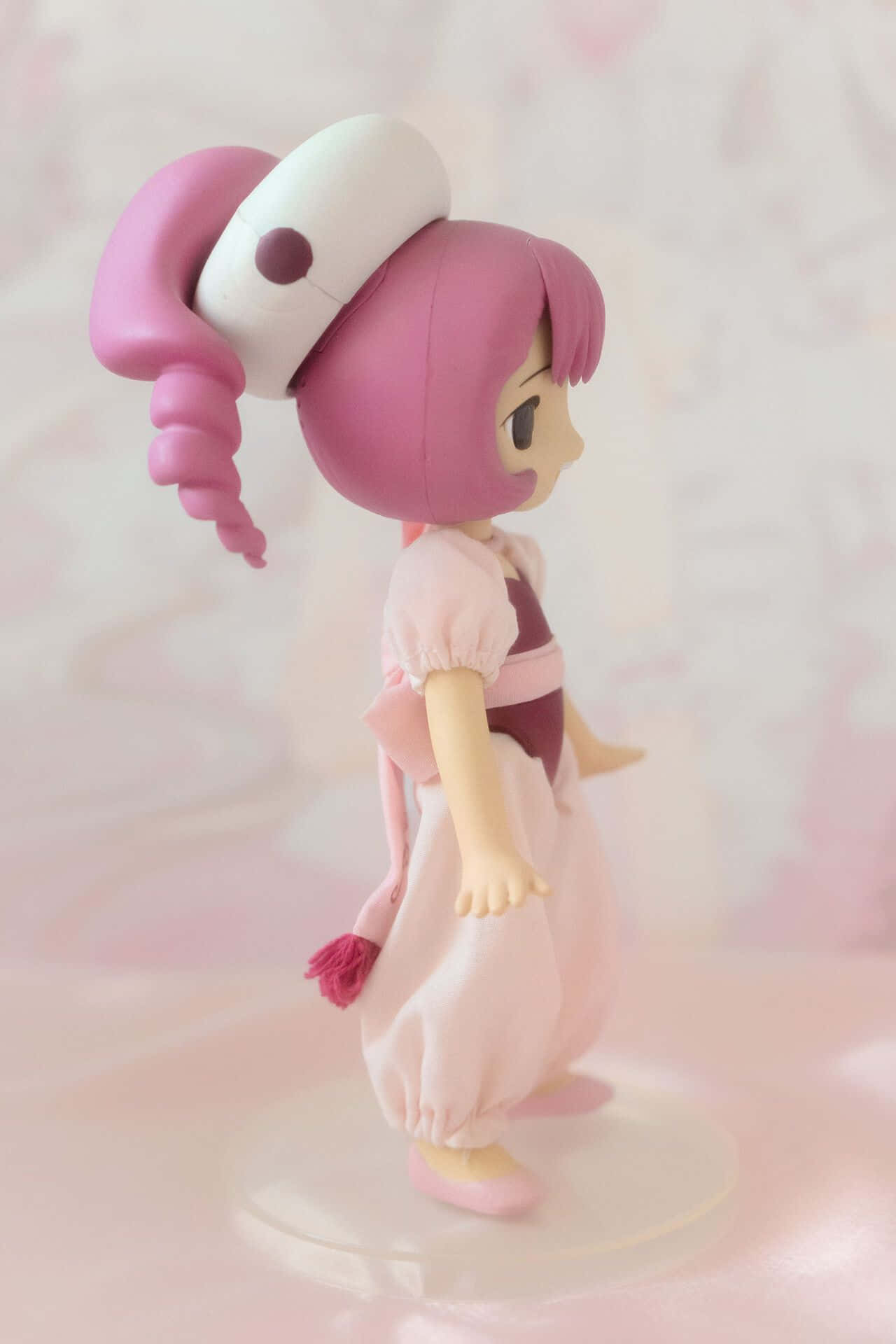  壁紙 — 一個粉紅色頭髮的動漫人偶穿著護士服，站在柔和的粉彩光線中，背景是模糊的粉紅色。