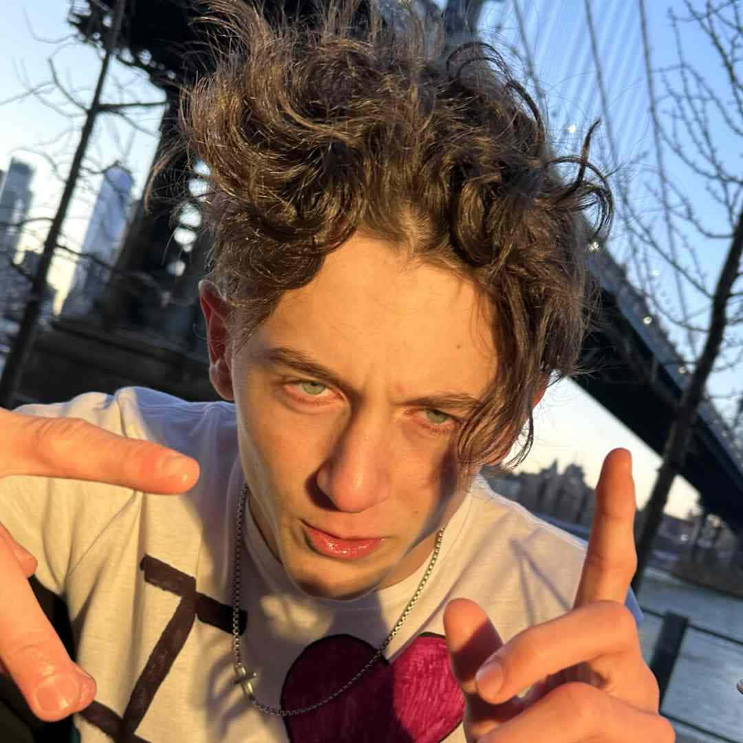  壁紙 — 一個頭髮凌亂的年輕男子，在黃金時段的城市橋樑背景下做出俏皮的表情和手勢。