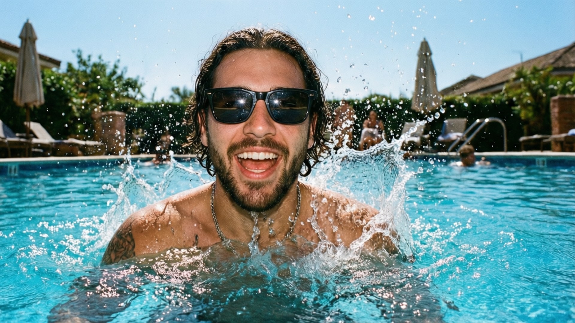 Pool Splash Summer 壁紙 — 一個頭髮濕透、戴著太陽眼鏡的男人在明亮的藍色泳池中，水花四濺，他開懷大笑。