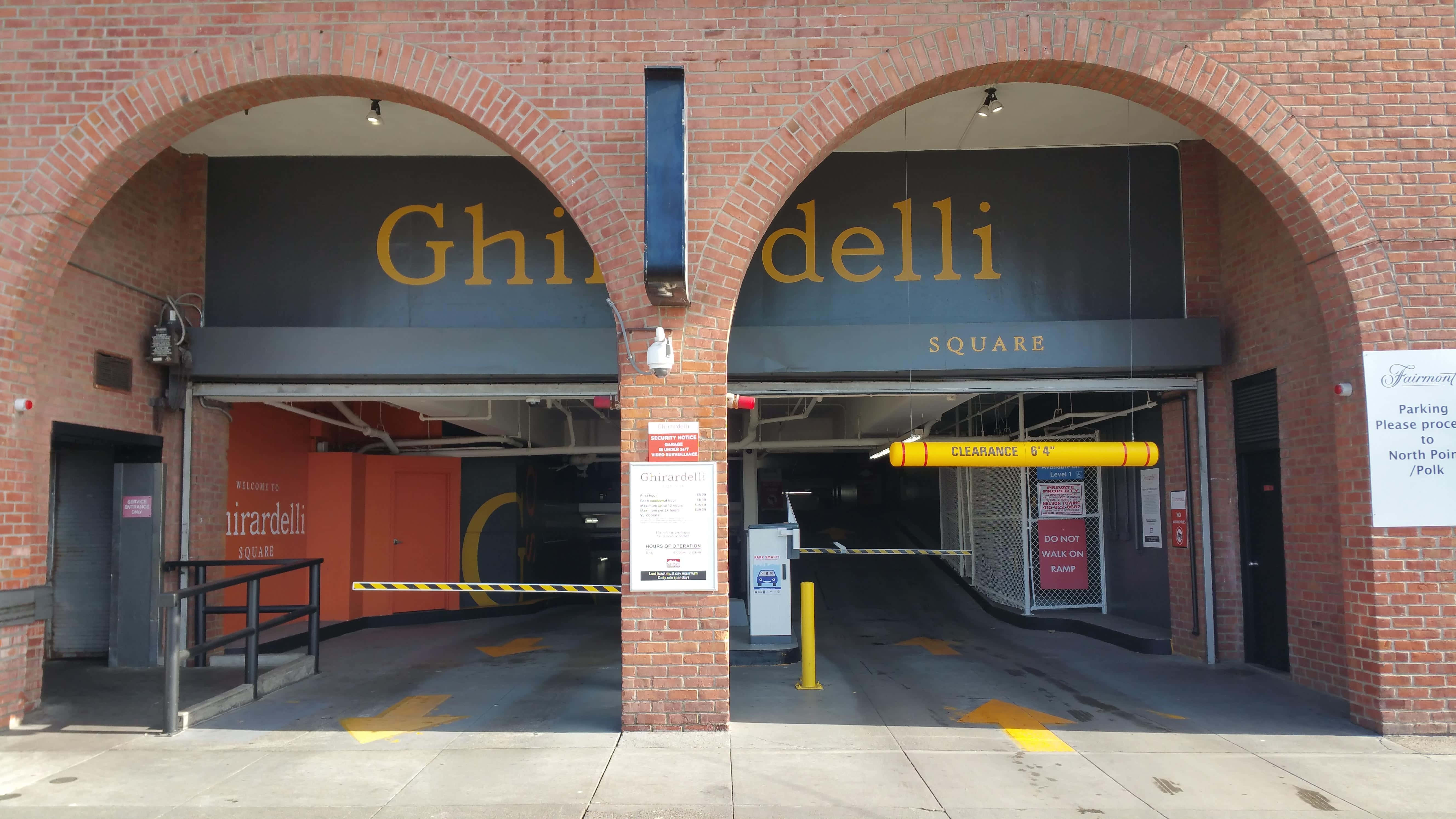 城市 桌布 壁紙 — Ghirardelli Square 停車場的磚拱入口，帶有黃色限高桿和路面方向箭頭。