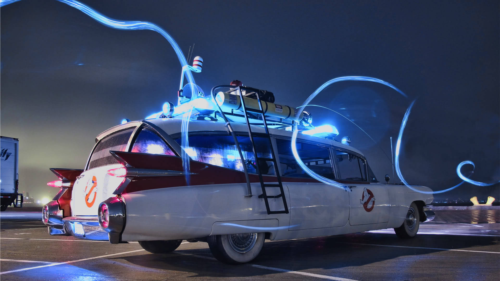 凱迪拉克 iPhone 桌布 壁紙 — Ghostbusters Ecto 1 汽車在夜間黑暗的停車場中發出藍色光芒的軌跡。