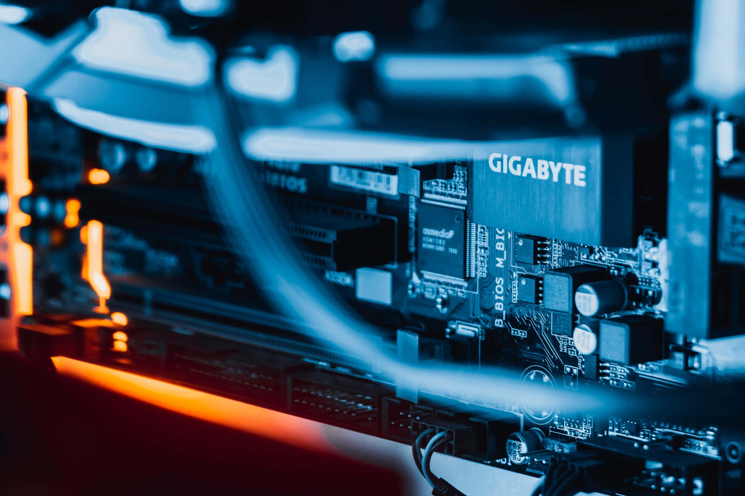 Gaming Servers 桌布 壁紙 — Gigabyte 主機板特寫，藍色和橙色 LED 燈光突顯複雜的電路。
