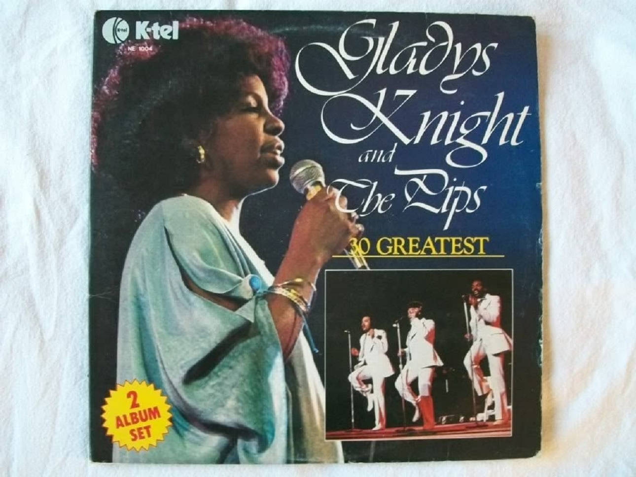 Album Cover 桌布 壁紙 — Gladys Knight 身穿藍綠色長袍，在復古專輯封面上對著麥克風唱歌，下方是她穿著白色西裝的樂隊。