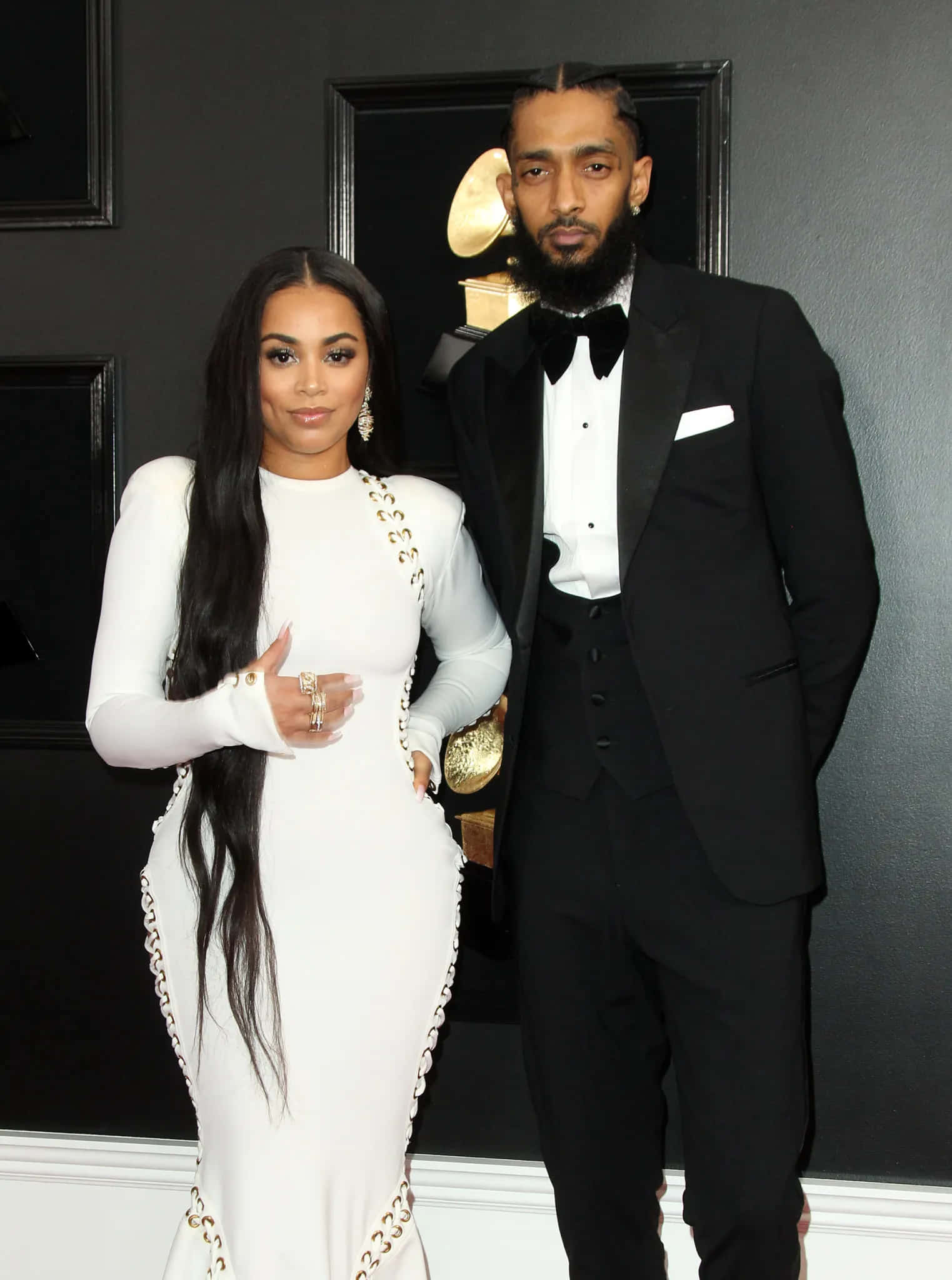 Lauren London 桌布 壁紙 — 一對魅力情侶穿著正式服裝，在深色牆壁前擺姿勢，身後有葛萊美獎獎座。
