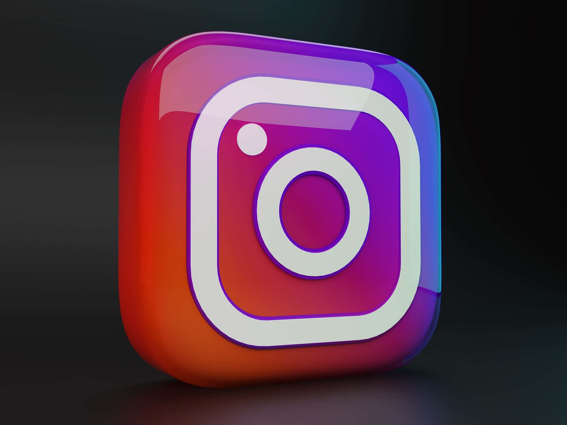  壁紙 — 一個帶有鮮豔漸層色彩的光澤3D渲染Instagram標誌圖標，置於深色背景上。