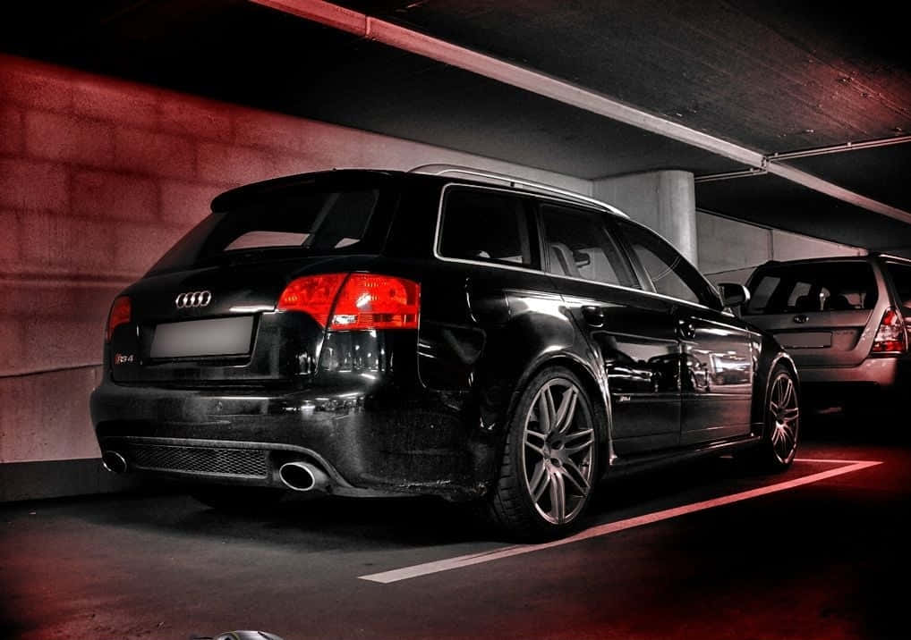 Audi Rs4 桌布 壁紙 — 一輛光澤黑色奧迪旅行車停在昏暗的地下車庫中，沐浴在紅色環境光下。
