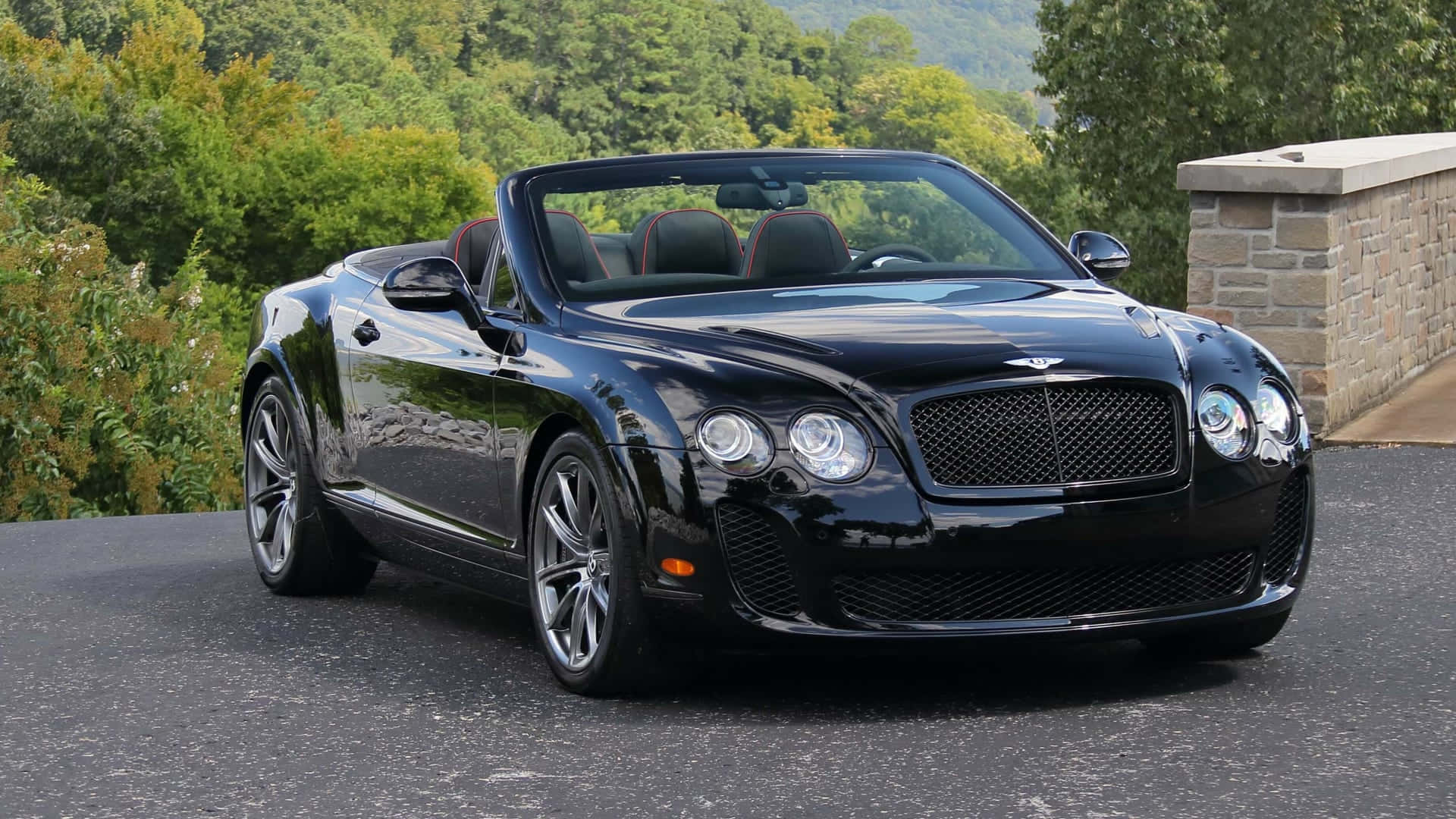 Bentley Continental Supersports 桌布 壁紙 — 一輛亮黑色賓利敞篷車停在柏油路上，背景有茂密的綠樹和石牆。