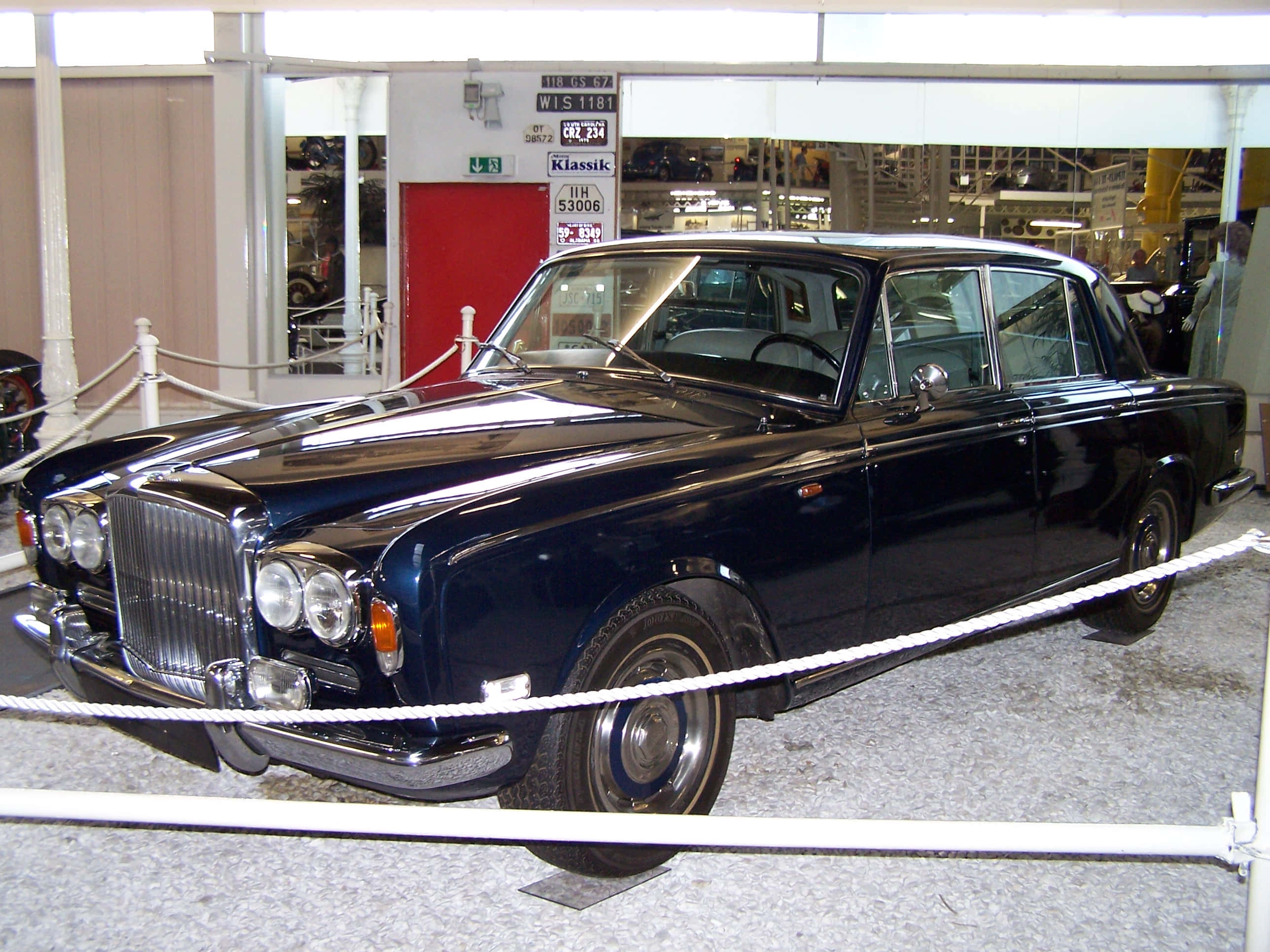 Bentley T1 桌布 壁紙 — 一輛光澤黑色經典勞斯萊斯在博物館內展示，配有白色繩索和明亮燈光。