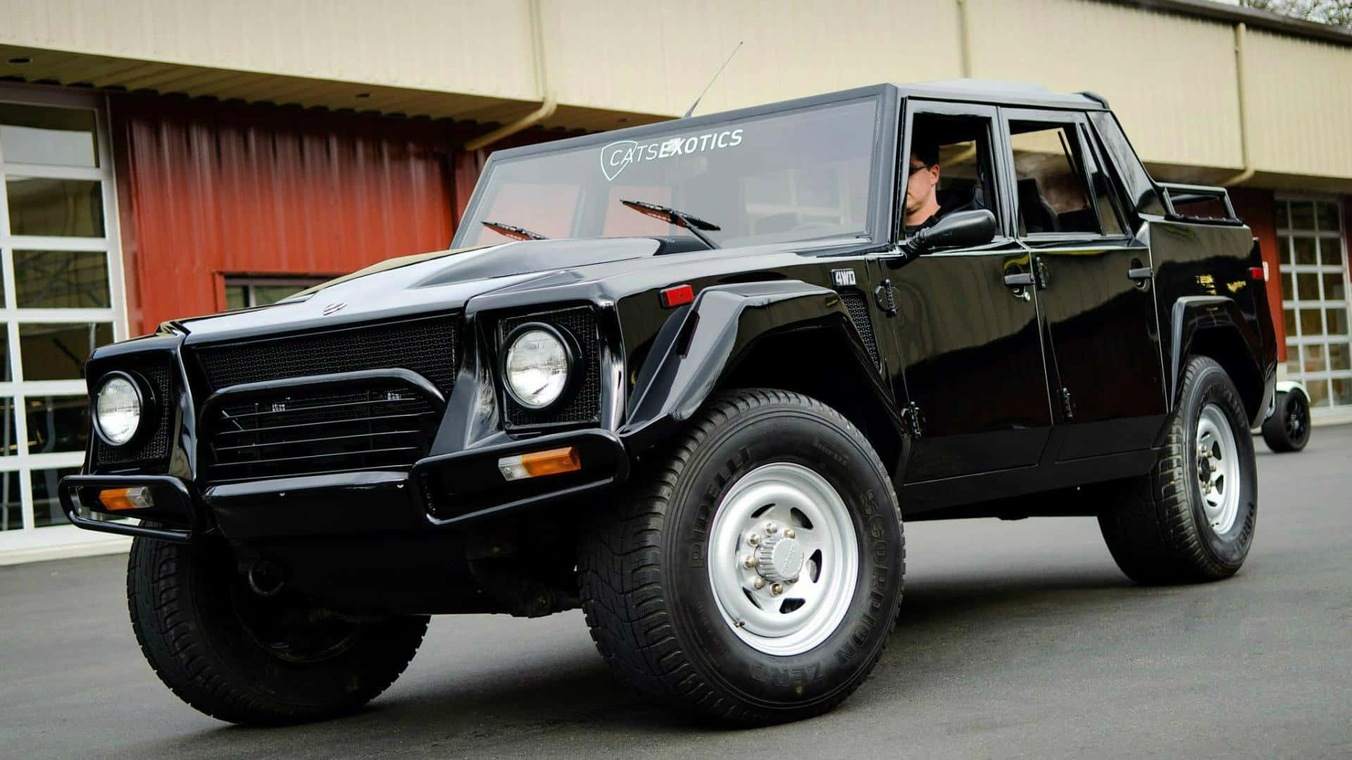 Lamborghini Lm002 桌布 壁紙 — 一輛亮黑色藍寶堅尼LM002豪華越野車停在車庫外，車內可見一人。