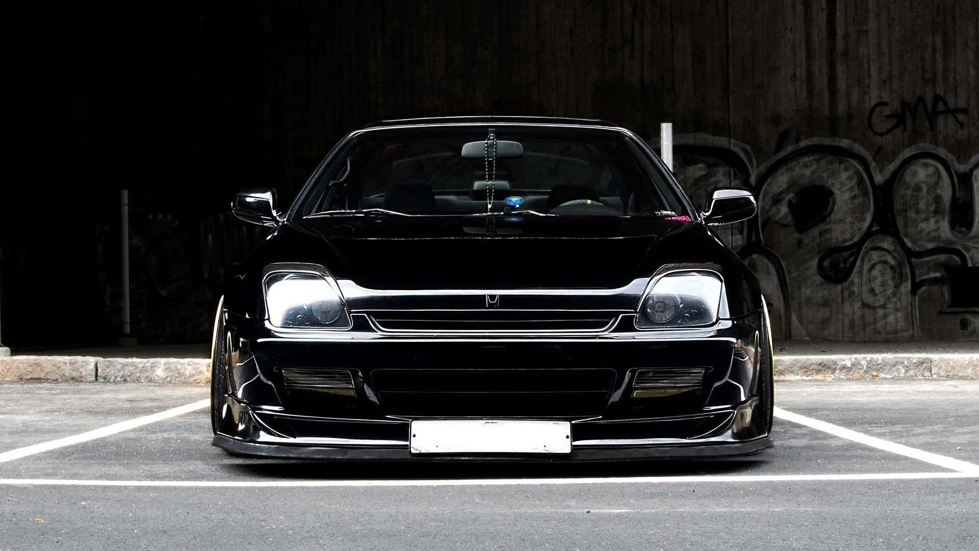 Honda Prelude 桌布 壁紙 — 一輛光澤黑色改裝跑車，帶有定制保險桿和降低的姿態，夜間停在一個塗鴉覆蓋的城市地塊中。