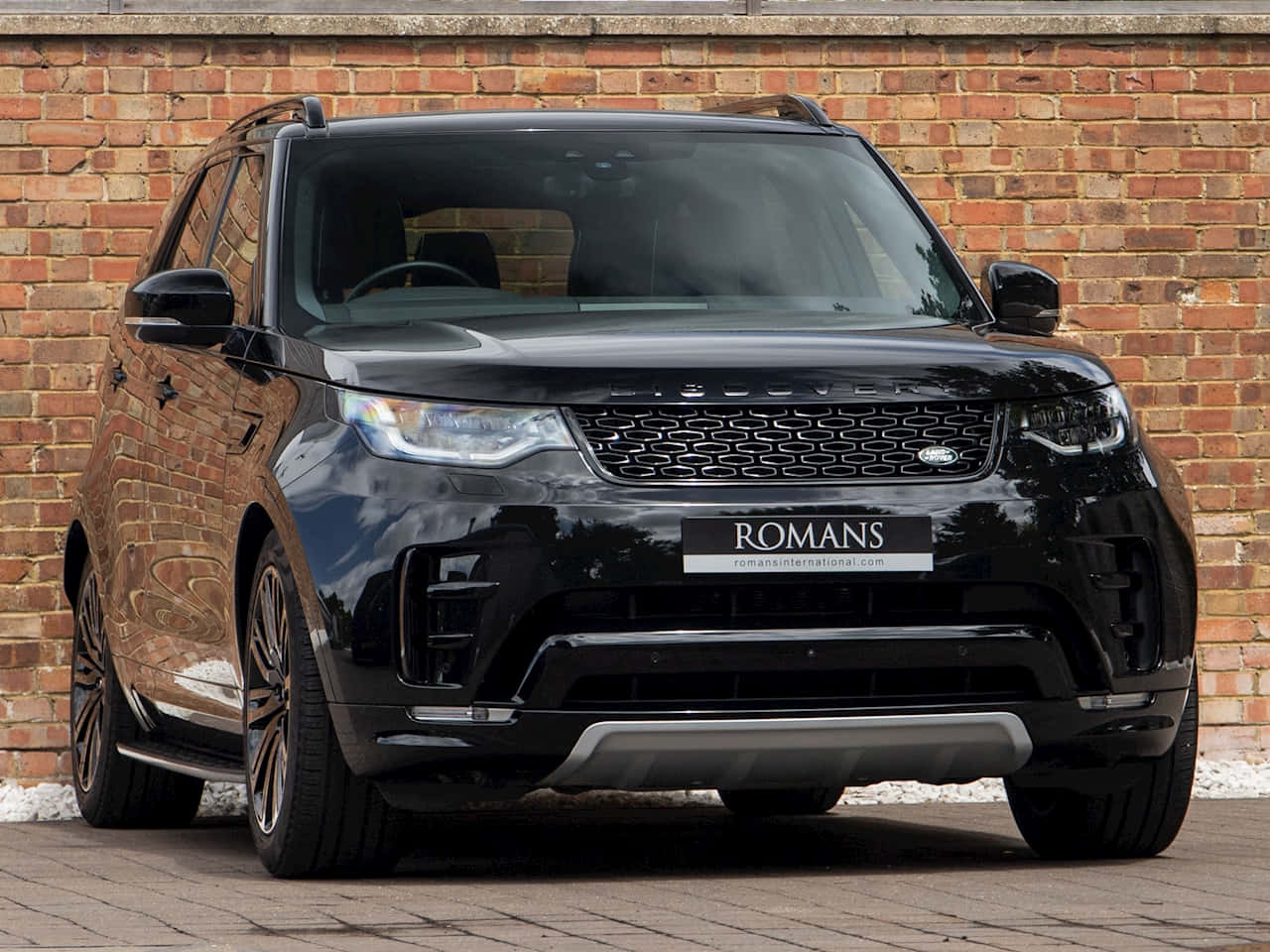 Land Rover Discovery 桌布 壁紙 — 一輛亮黑色Range Rover Sport停放在紅磚牆前的鋪砌地面上。