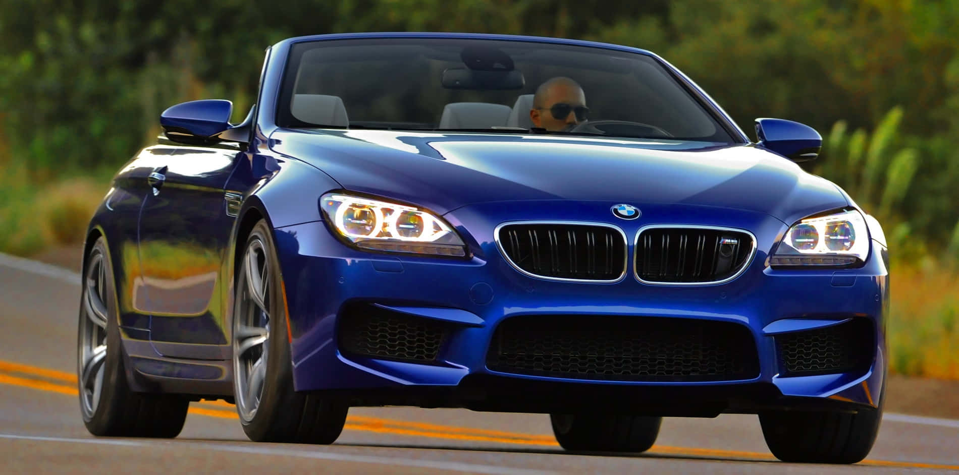 Bmw M6 桌布 壁紙 — 一輛閃亮藍色BMW M6敞篷跑車在陽光明媚的道路上疾馳，司機戴著太陽眼鏡。