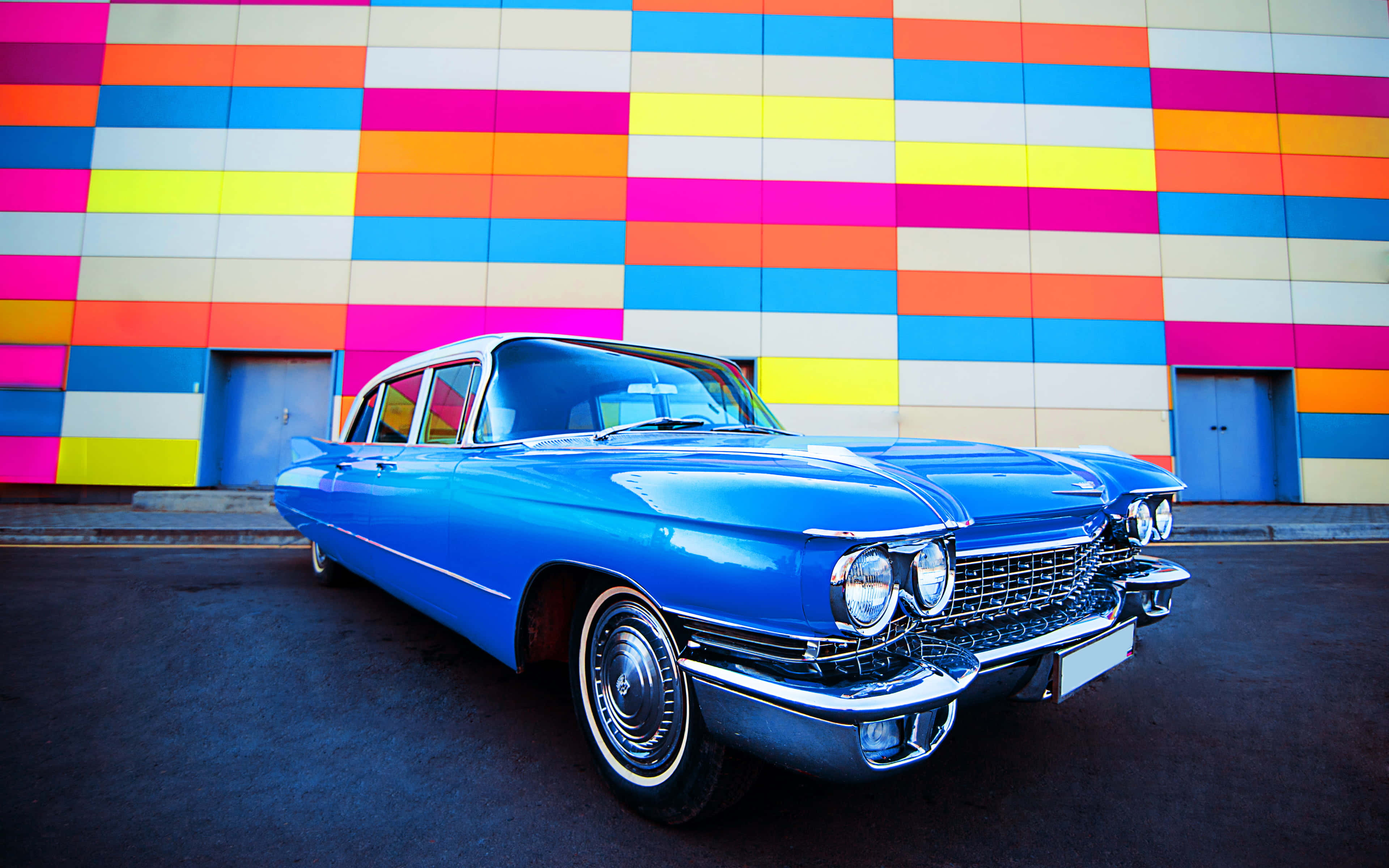 Cadillac Fleetwood 桌布 壁紙 — 一輛閃亮的藍色經典汽車停在一幅充滿活力的多色幾何牆前。