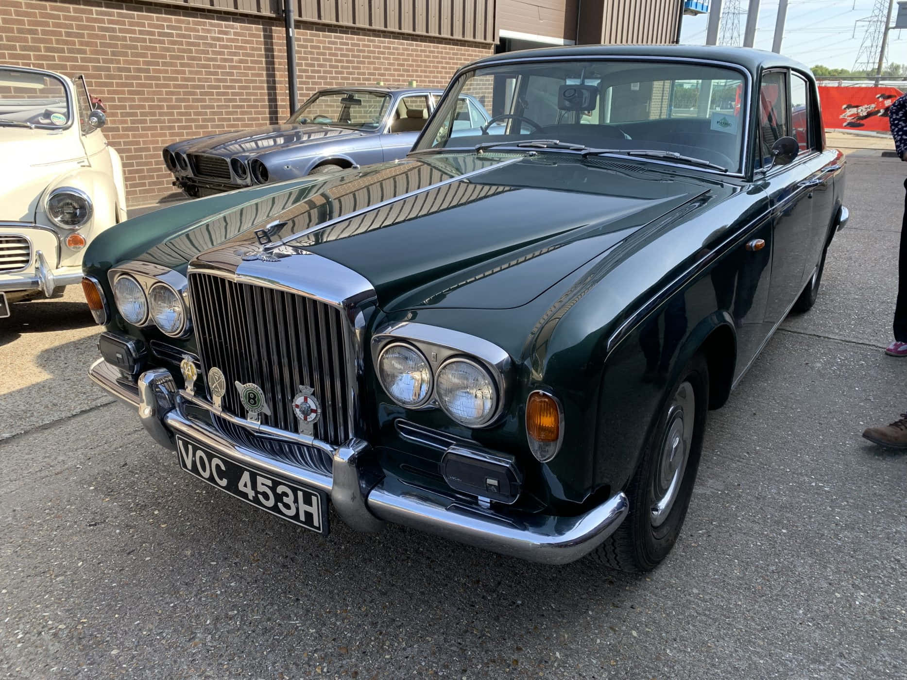 Bentley T1 桌布 壁紙 — 一輛光澤深綠色復古賓利S3轎車在明亮的日光下閃閃發光，停在瀝青停車場上其他經典汽車旁邊。
