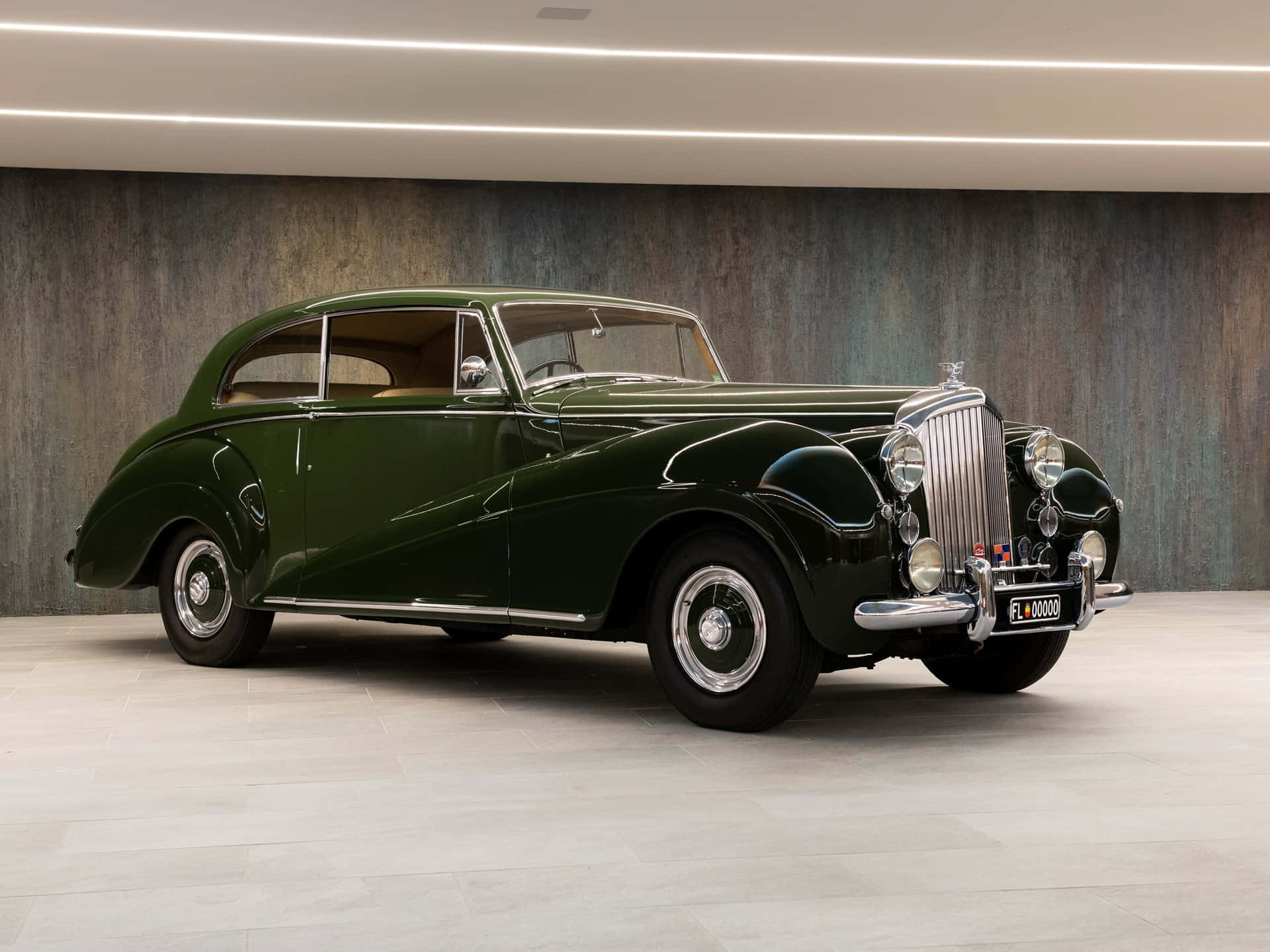 Bentley Mark Vi 桌布 壁紙 — 一輛光澤深綠色復古賓利轎車在明亮的攝影棚燈光下，映襯著紋理灰色牆壁閃閃發光。