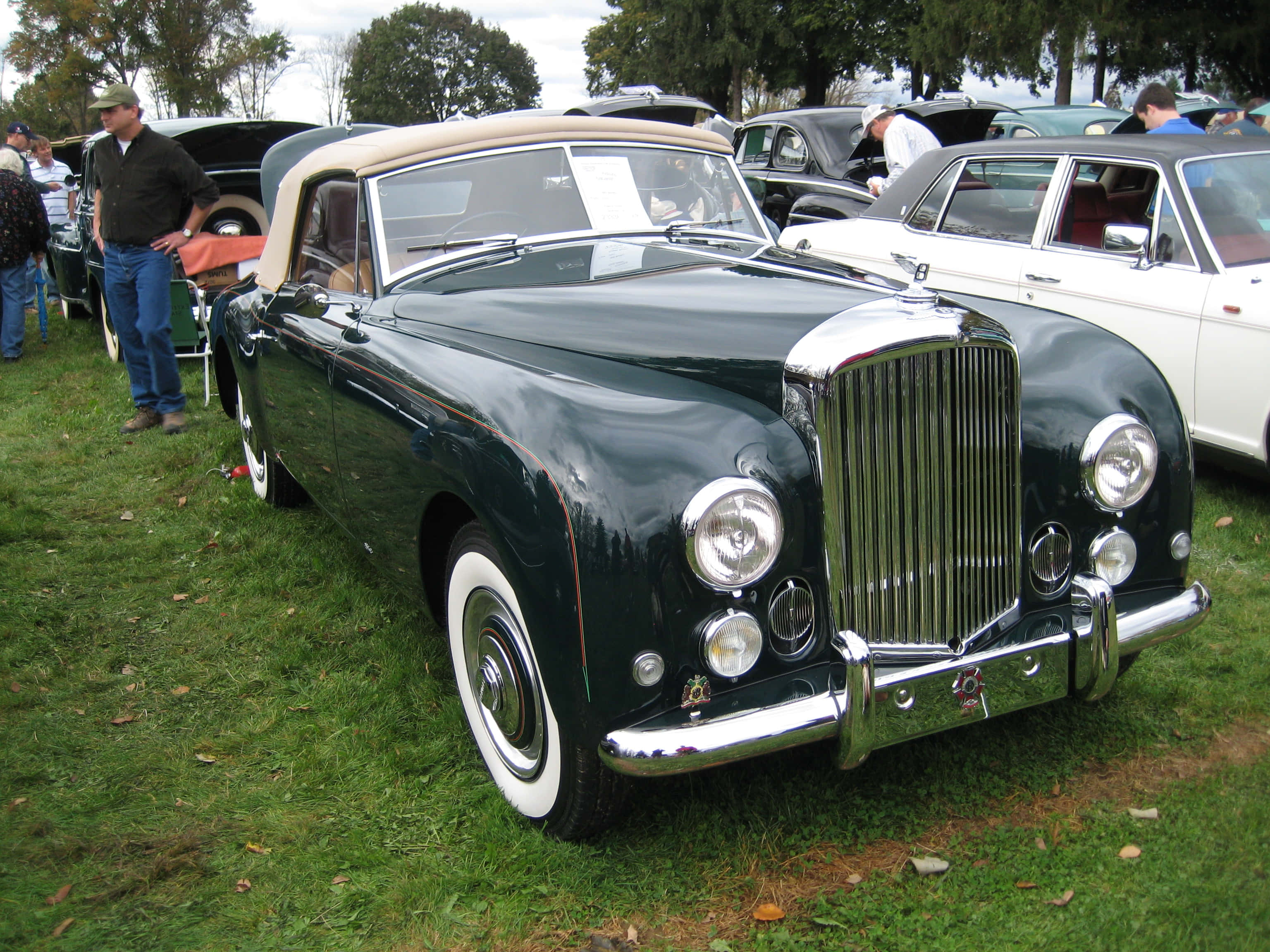 Bentley Mark Vi 桌布 壁紙 — 一輛光澤深綠色復古敞篷車配備白色輪胎，在多雲的天空下於戶外經典車展中閃閃發光。