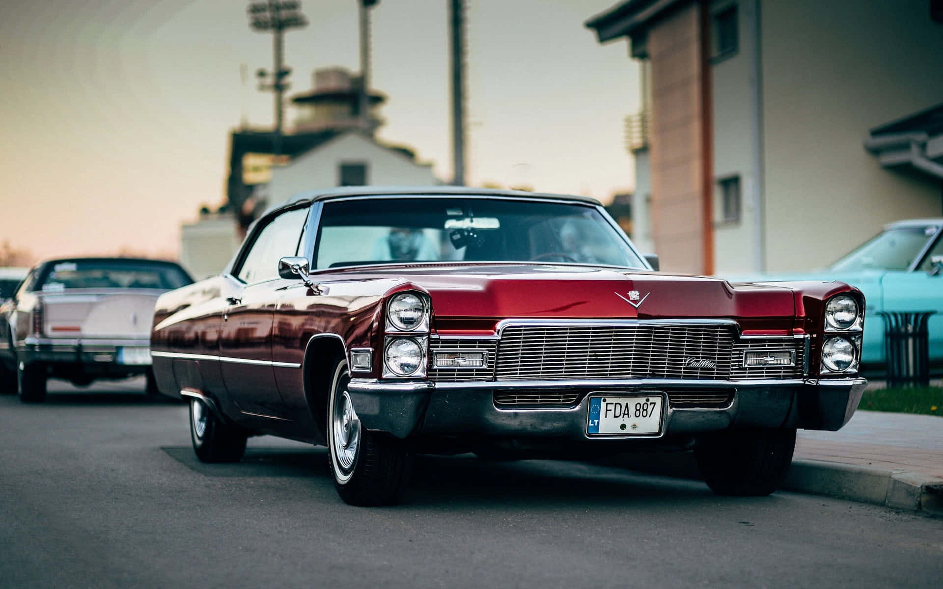 Cadillac Eldorado 桌布 壁紙 — 一輛光澤的栗色經典凱迪拉克轎車在日落時停放在街上，附近有復古汽車。