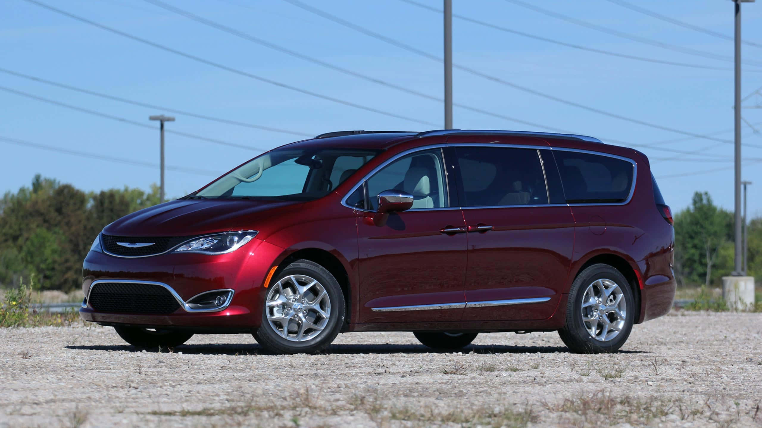 Chrysler Pacifica 桌布 壁紙 — 一輛光澤的栗色小型貨車停放在碎石上，背景是晴朗的藍天、電線和樹木。