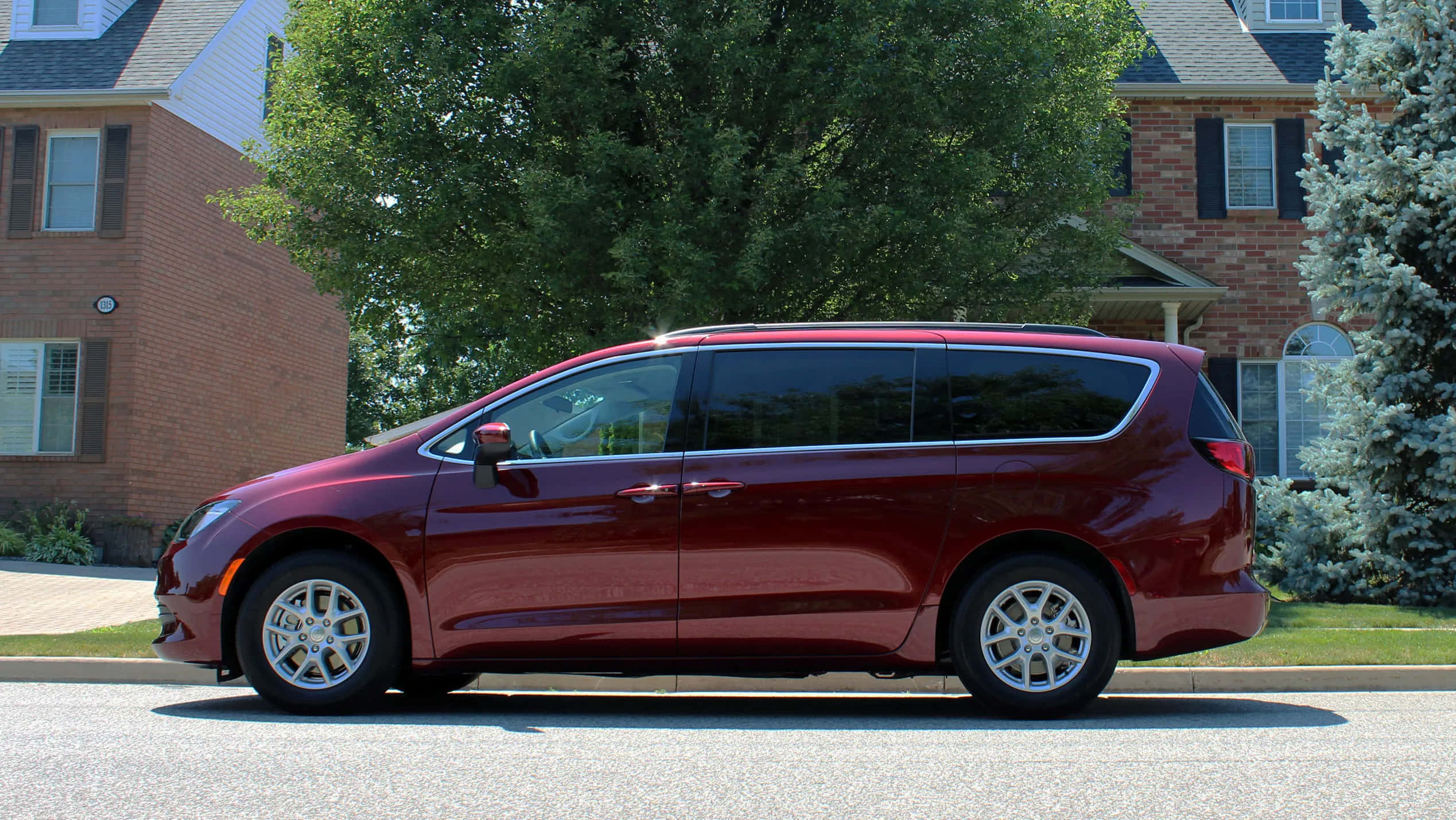 Chrysler Voyager 桌布 壁紙 — 一輛光澤的栗色小型貨車停放在郊區街道上，旁邊是磚房和綠樹，在明亮的日光下。
