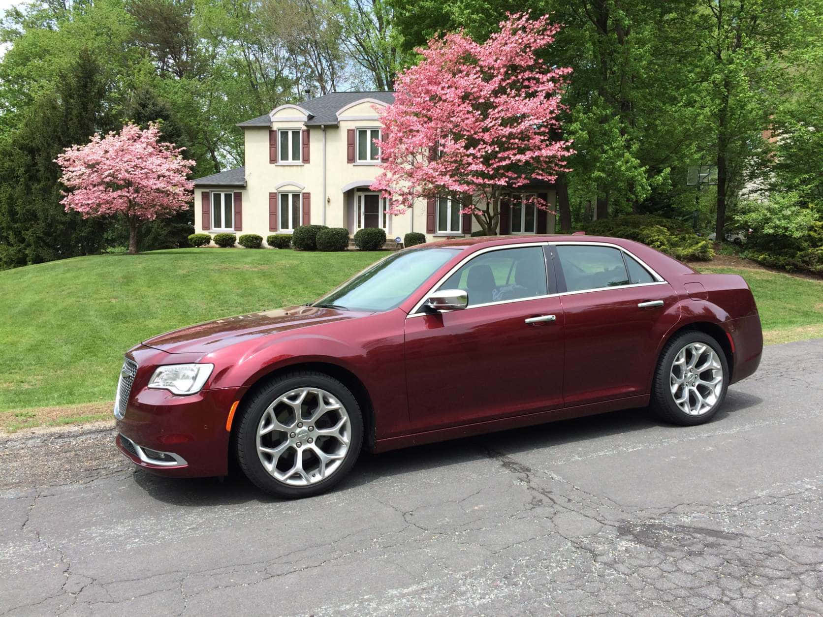 Chrysler 300 桌布 壁紙 — 一輛亮面栗色轎車停在龜裂的車道上，前方是米色房屋，周圍環繞著盛開的粉紅色櫻花樹。