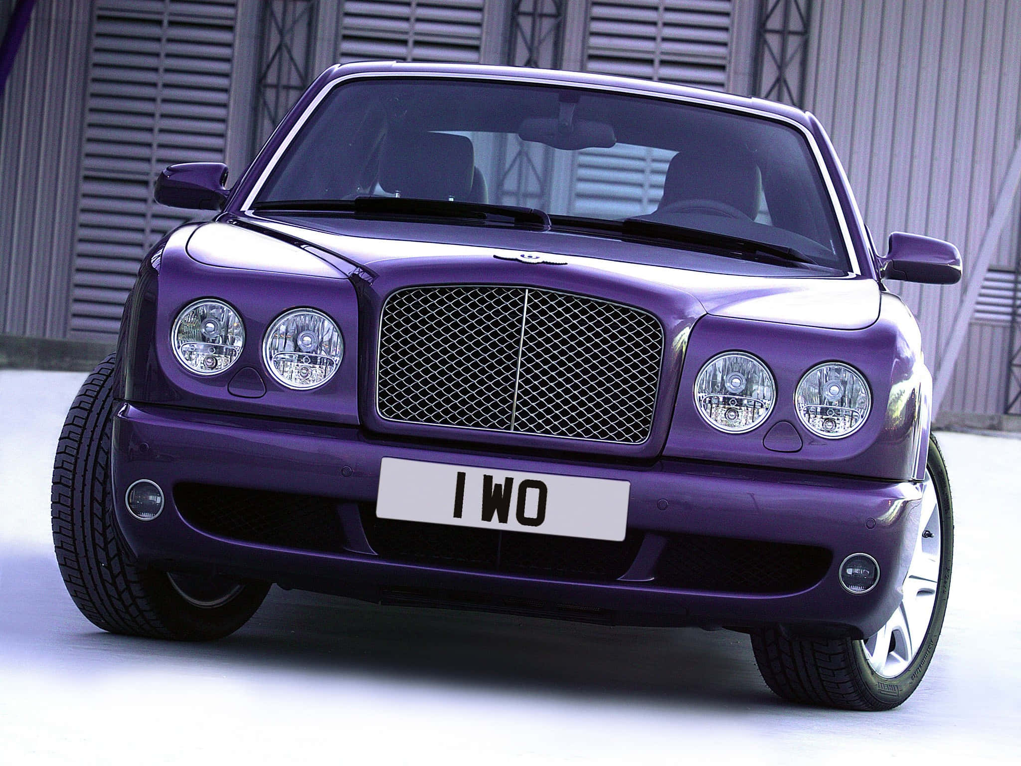 Bentley Arnage 桌布 壁紙 — 一輛光澤的紫色 Bentley Arnage，帶有鍍鉻格柵和圓形頭燈，停在金屬百葉窗建築前。