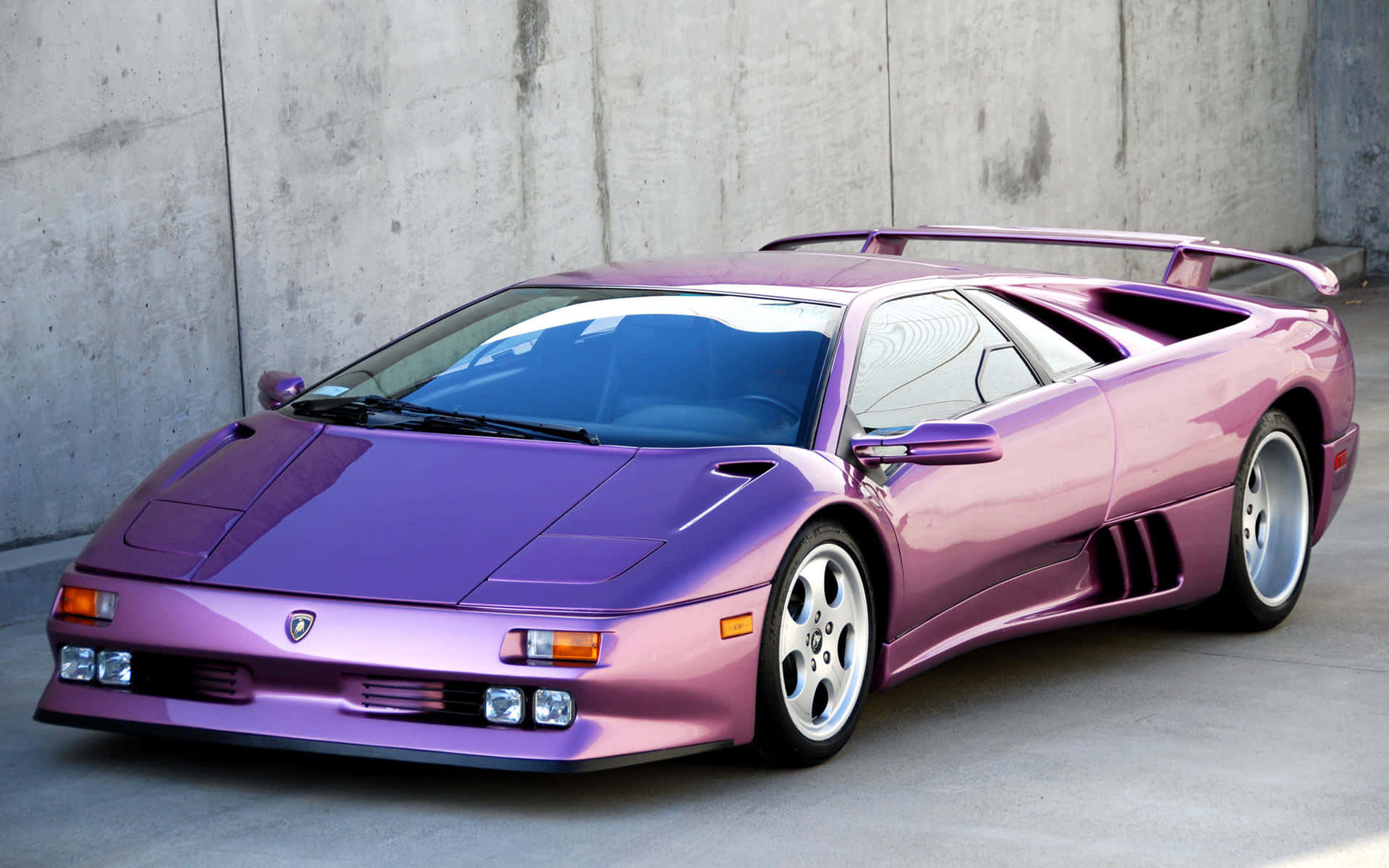 Lamborghini Diablo 桌布 壁紙 — 一輛光澤紫色藍寶堅尼 Diablo 跑車在明亮日光下停靠在混凝土牆邊。