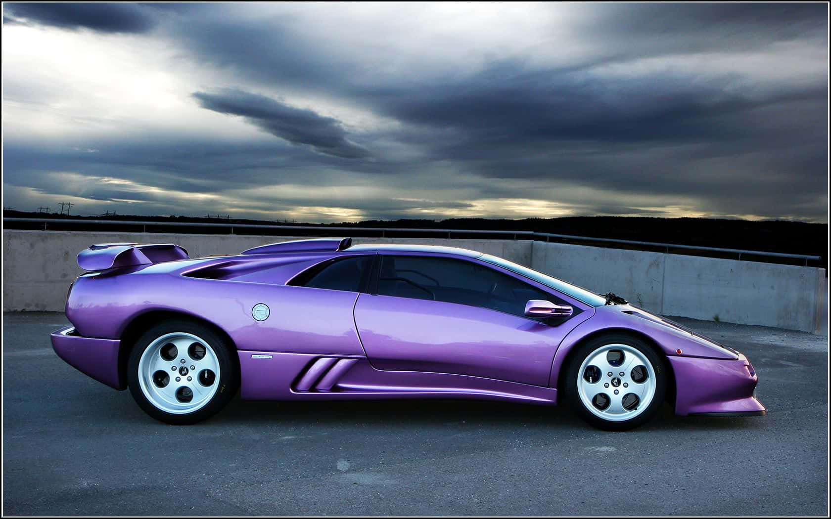 Lamborghini Diablo 桌布 壁紙 — 一輛光澤的紫色藍寶堅尼Diablo跑車停泊在天橋上，背景是黃昏時分戲劇性的暴風雨天空。