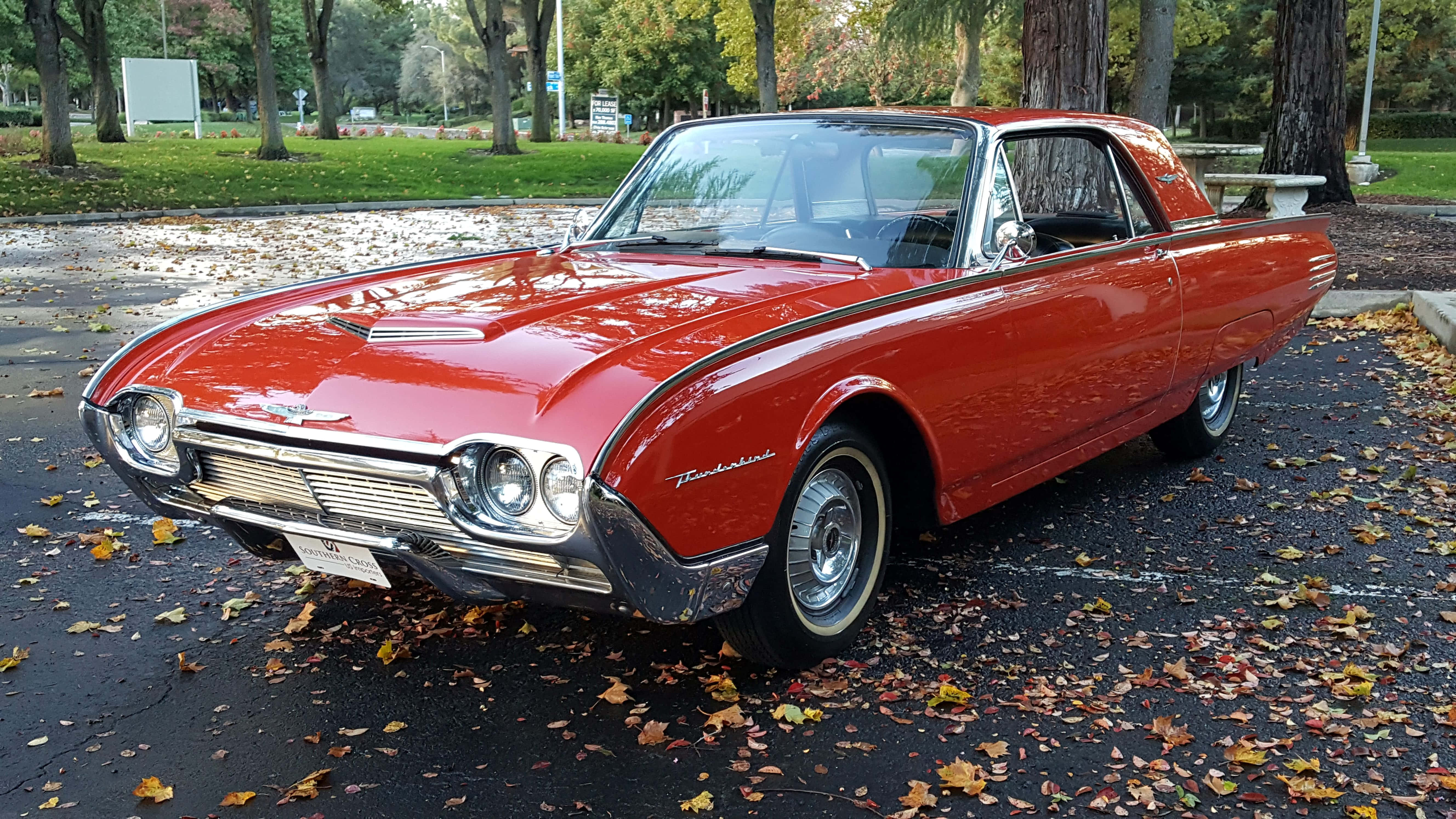 Ford Thunderbird 桌布 壁紙 — 一輛閃亮的紅色1960年代福特雷鳥經典汽車停放在濕漉漉的瀝青停車場上，散落著秋天的落葉。