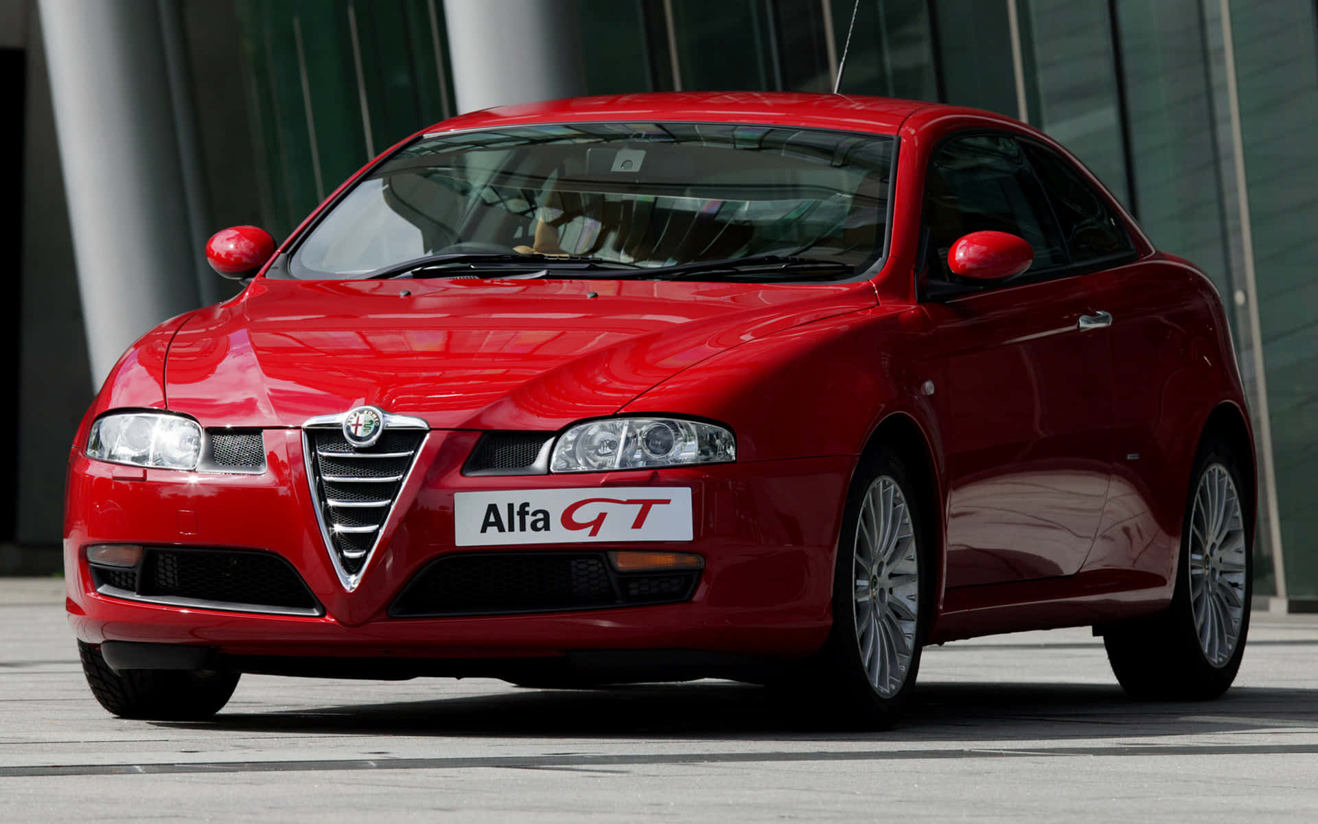 Alfa Romeo Gt 桌布 壁紙 — 一輛亮紅色的Alfa GT跑車停放在現代玻璃建築前，在晴朗的日子裡。