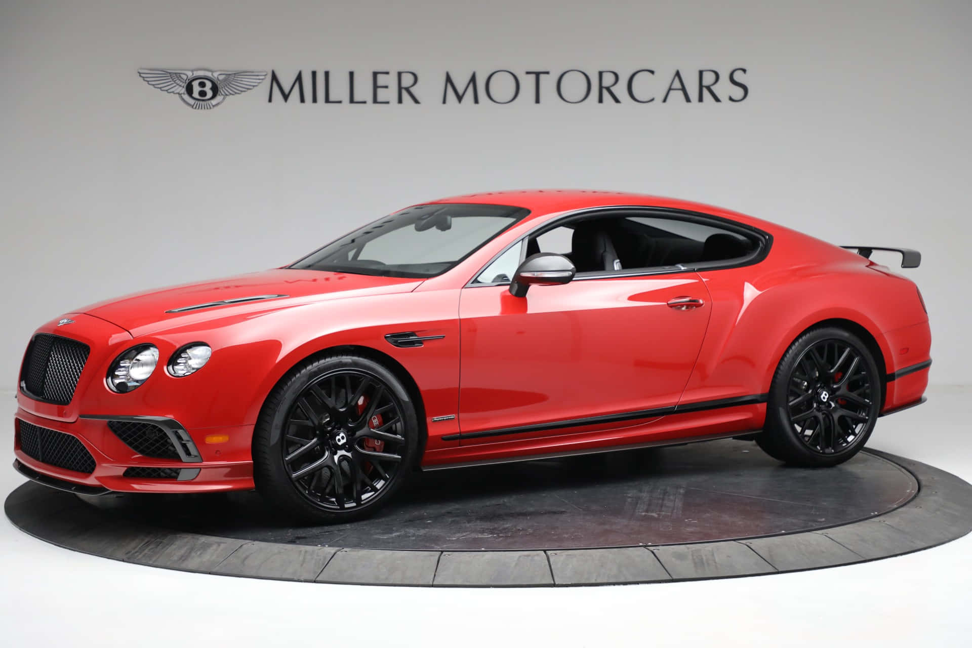 Bentley Continental Supersports 桌布 壁紙 — 一輛亮紅色的賓利 Continental GT Speed 在工作室燈光下於圓形平台上閃耀，背景有 Miller Motorcars 標誌。
