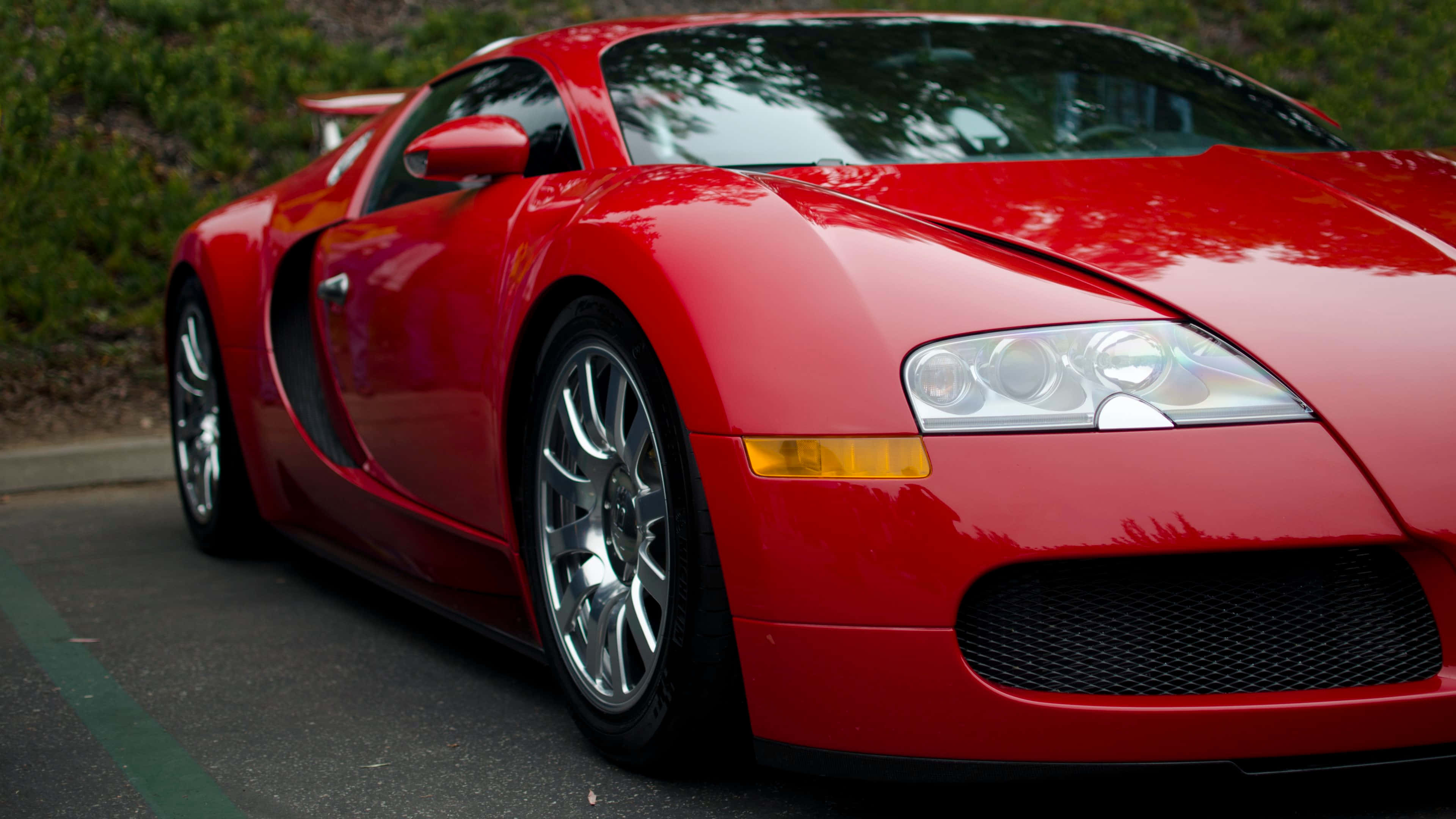 Bugatti Veyron 桌布 壁紙 — 一輛光澤的紅色Bugatti Veyron跑車停在瀝青路上，背景有綠色樹葉。