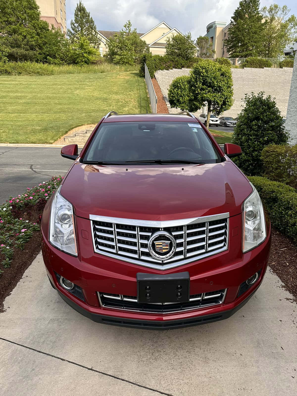 Cadillac Srx 桌布 壁紙 — 一輛亮紅色的Cadillac SRX在混凝土車道上向前，背景是修剪整齊的綠色草坪和樹木。