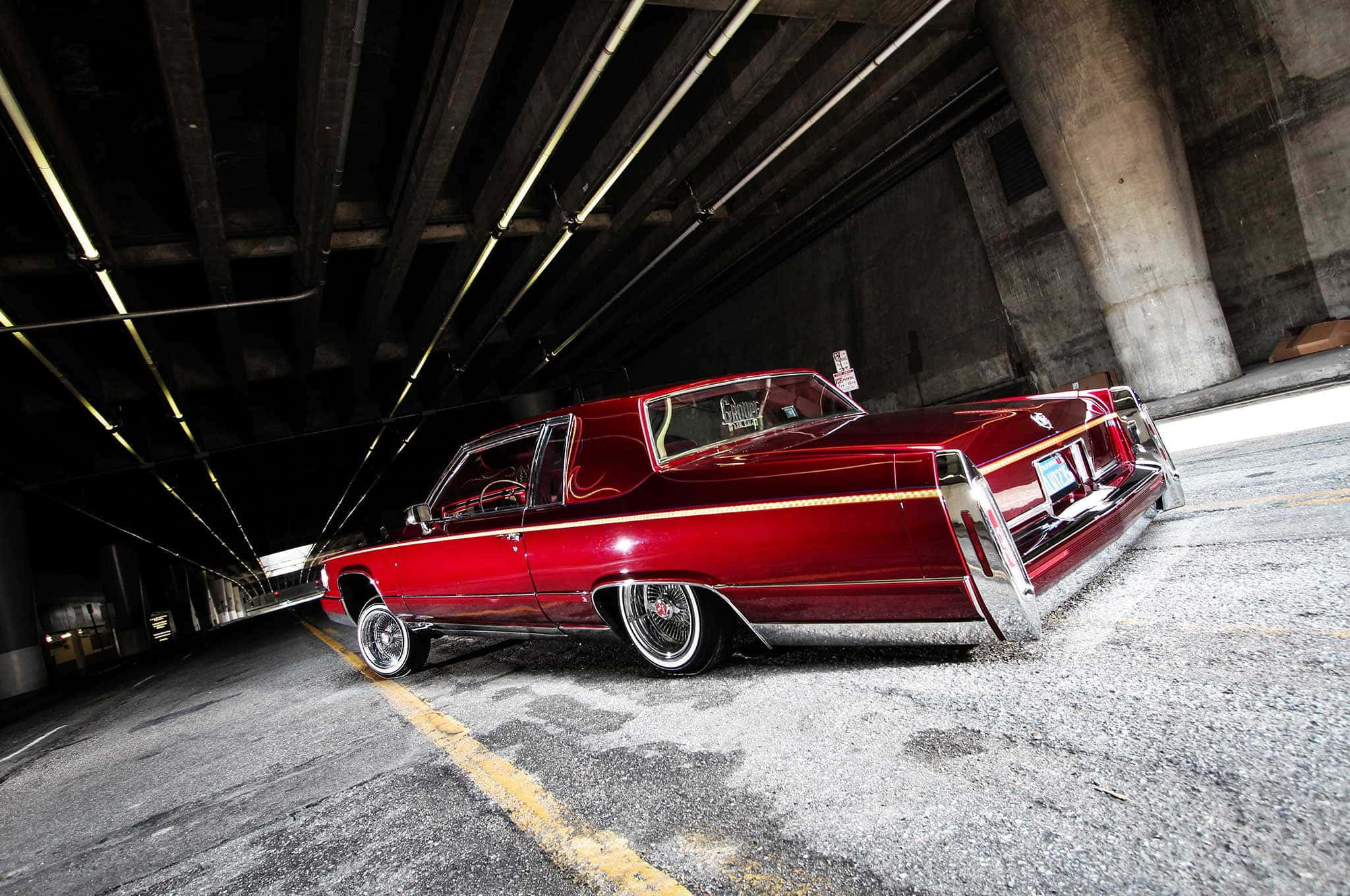 Cadillac Deville 桌布 壁紙 — 一輛光澤的紅色經典低底盤汽車停在混凝土天橋下，帶有戲劇性的燈光。